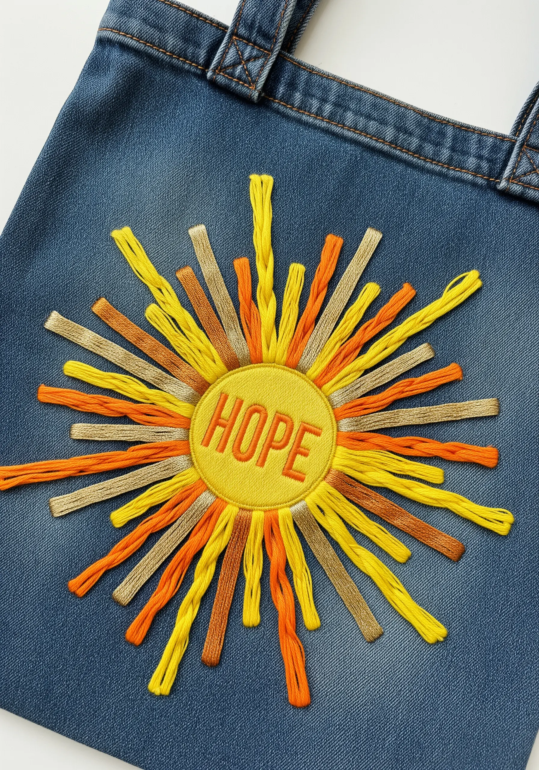 A sunburst embroidered with long yellow, orange, and tan stitches with the word 'HOPE'.