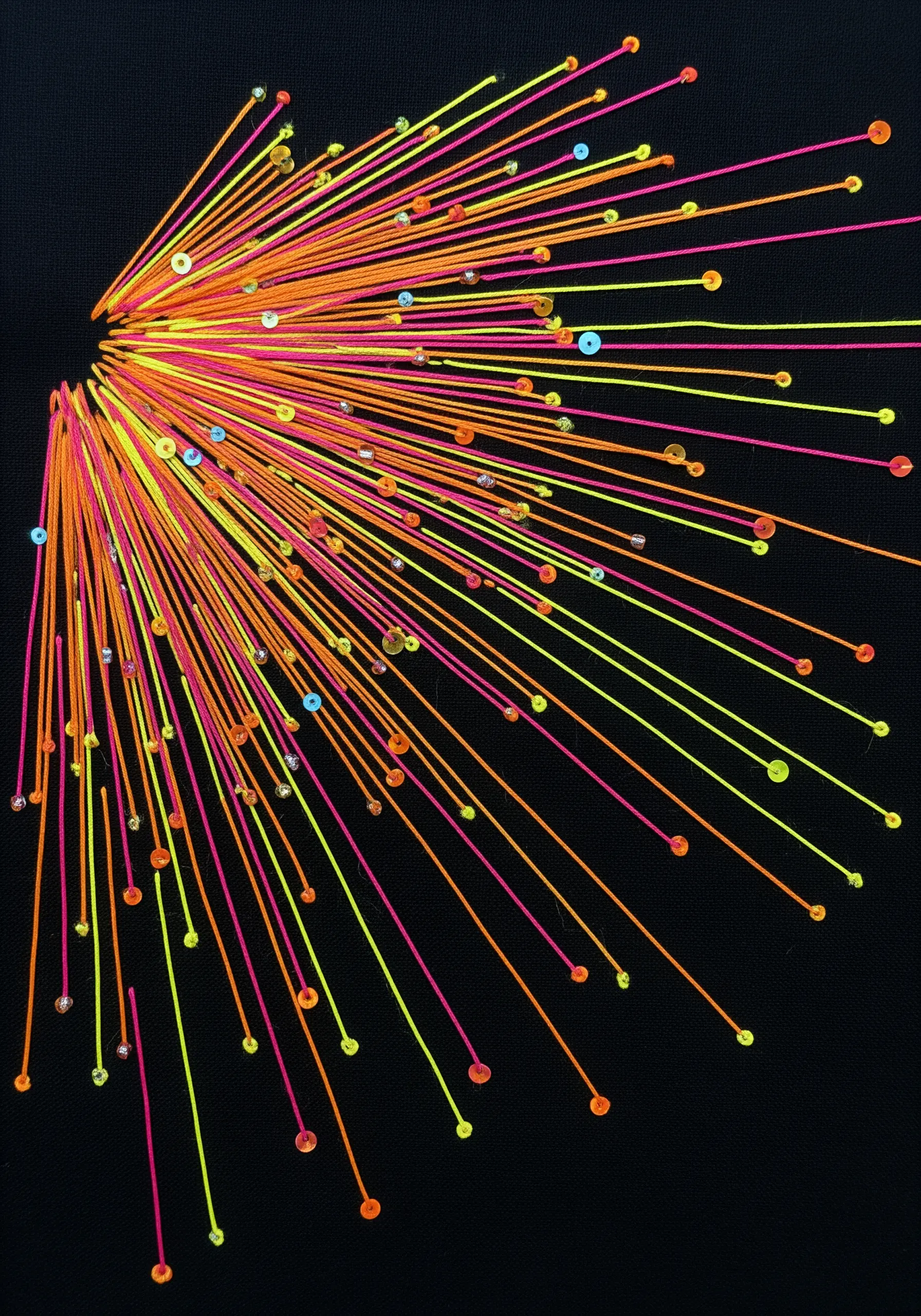 An explosion of radiating straight stitches in neon orange, yellow, and pink on black fabric.