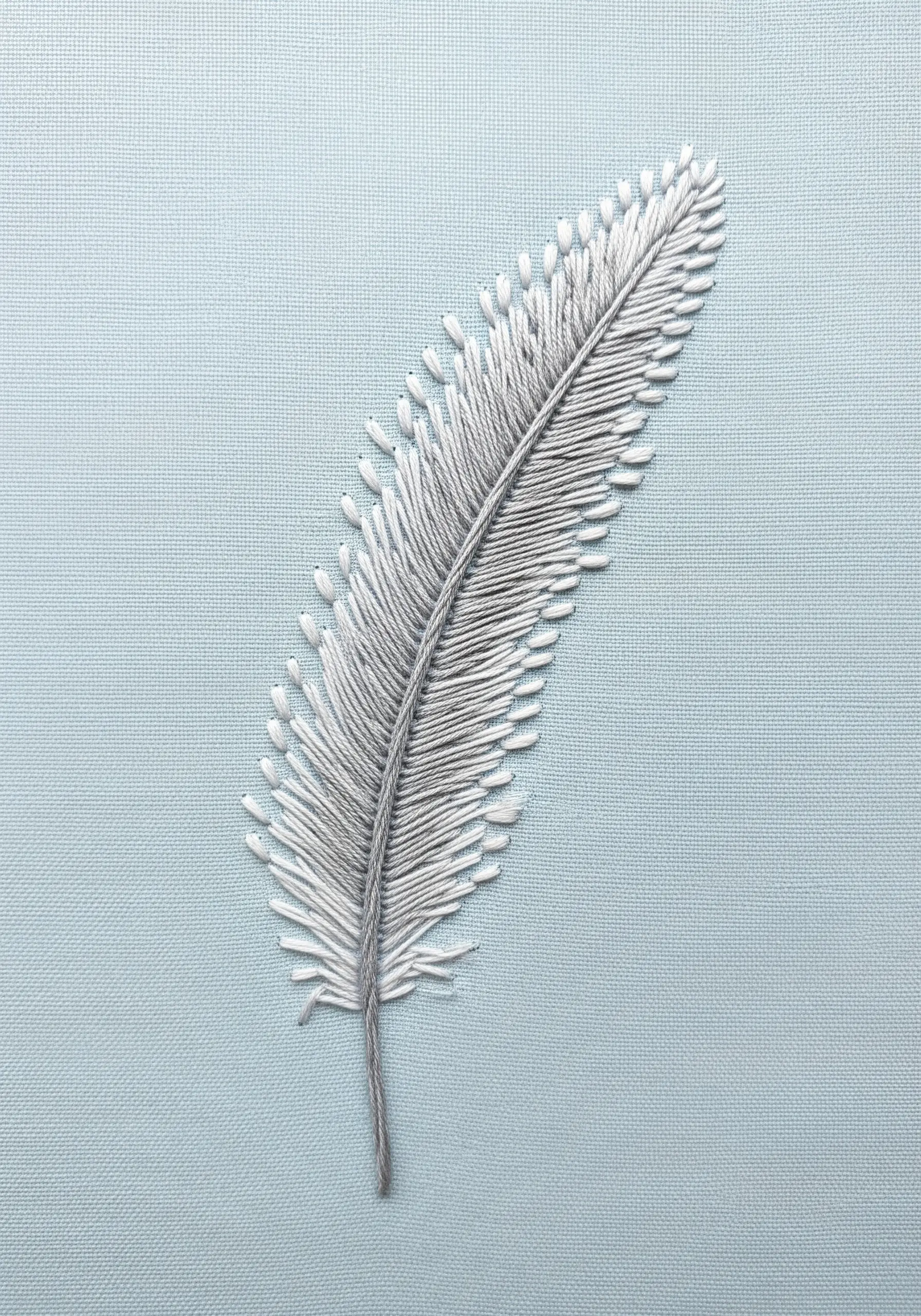 A realistic white and grey feather embroidered on light blue fabric.