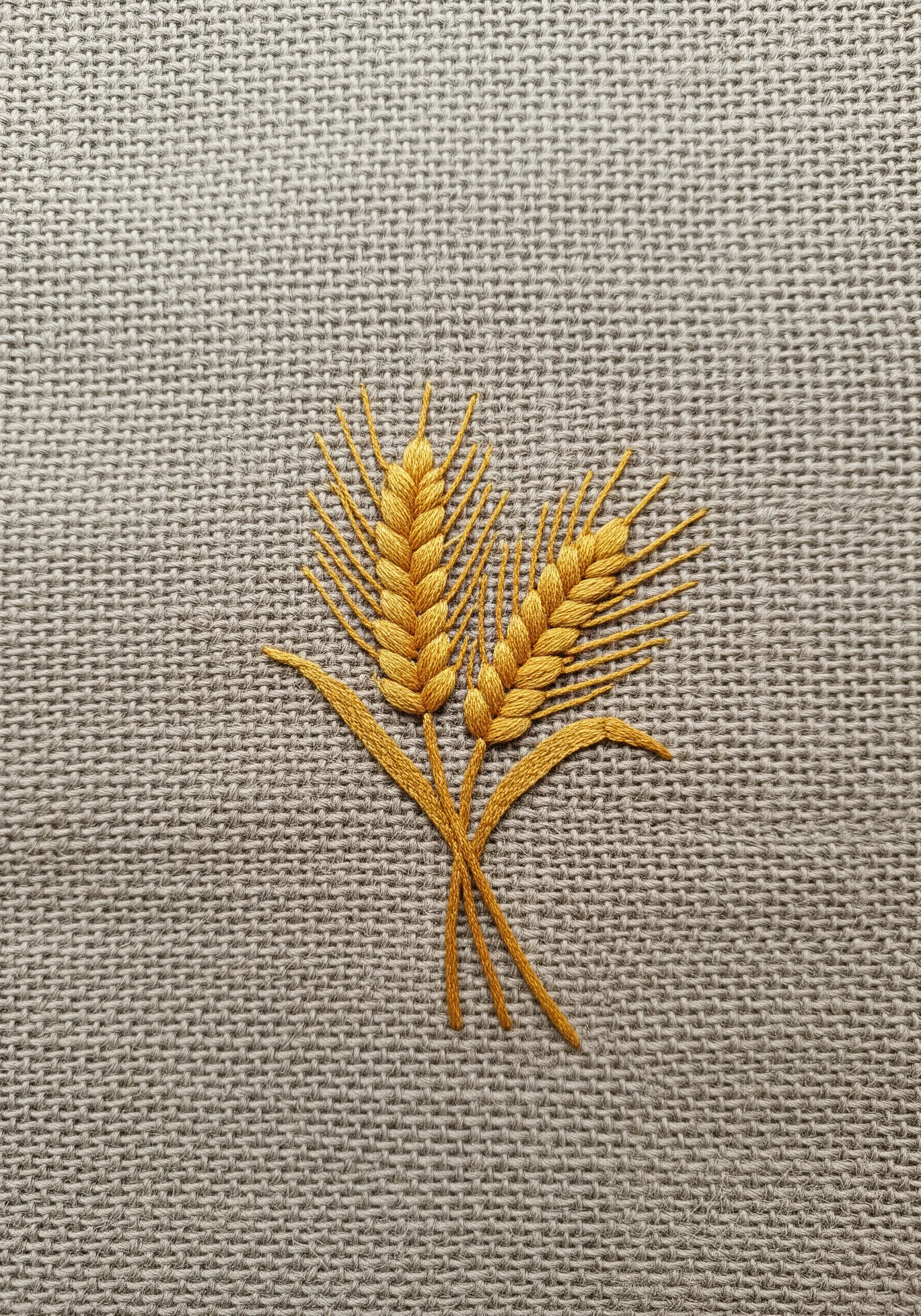 Two stalks of golden wheat embroidered on a textured linen background.