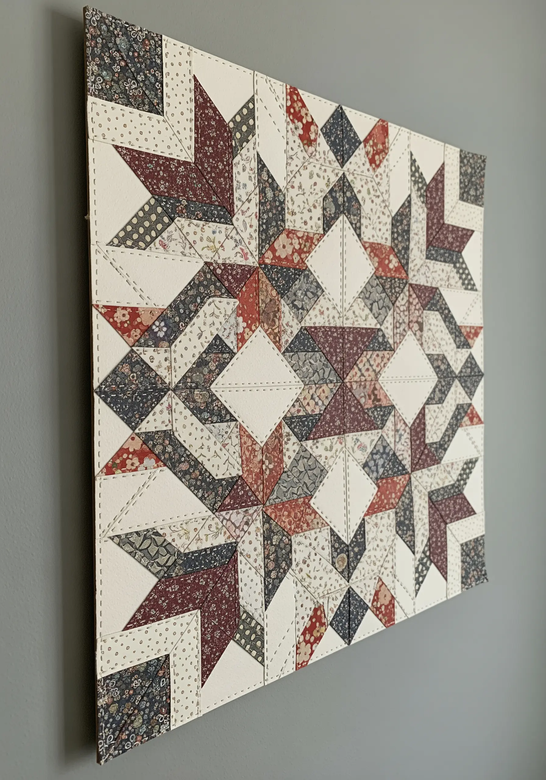 A quilt star pattern made from different patterned papers, with white running stitches along the seams.