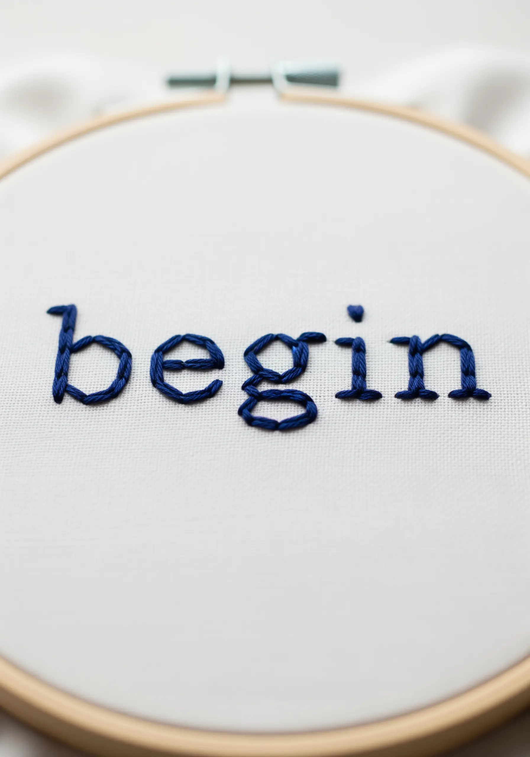 The word 'begin' embroidered in a dark blue typewriter-style font.