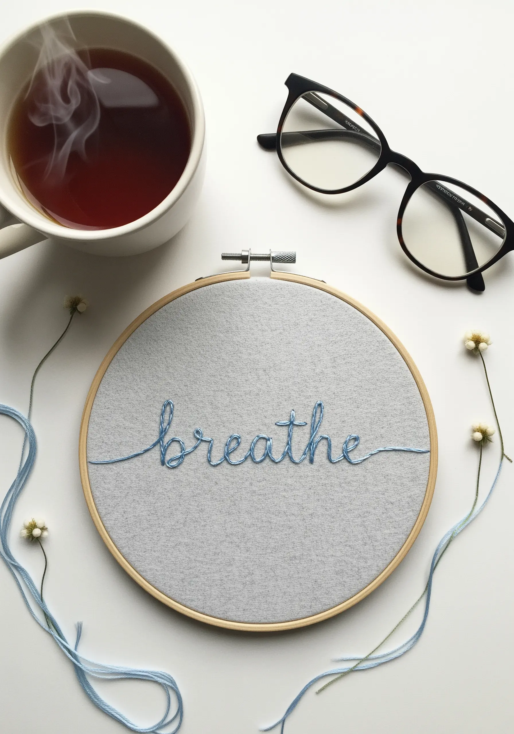 The word “breathe” in delicate blue whipped backstitch on a grey felt background.
