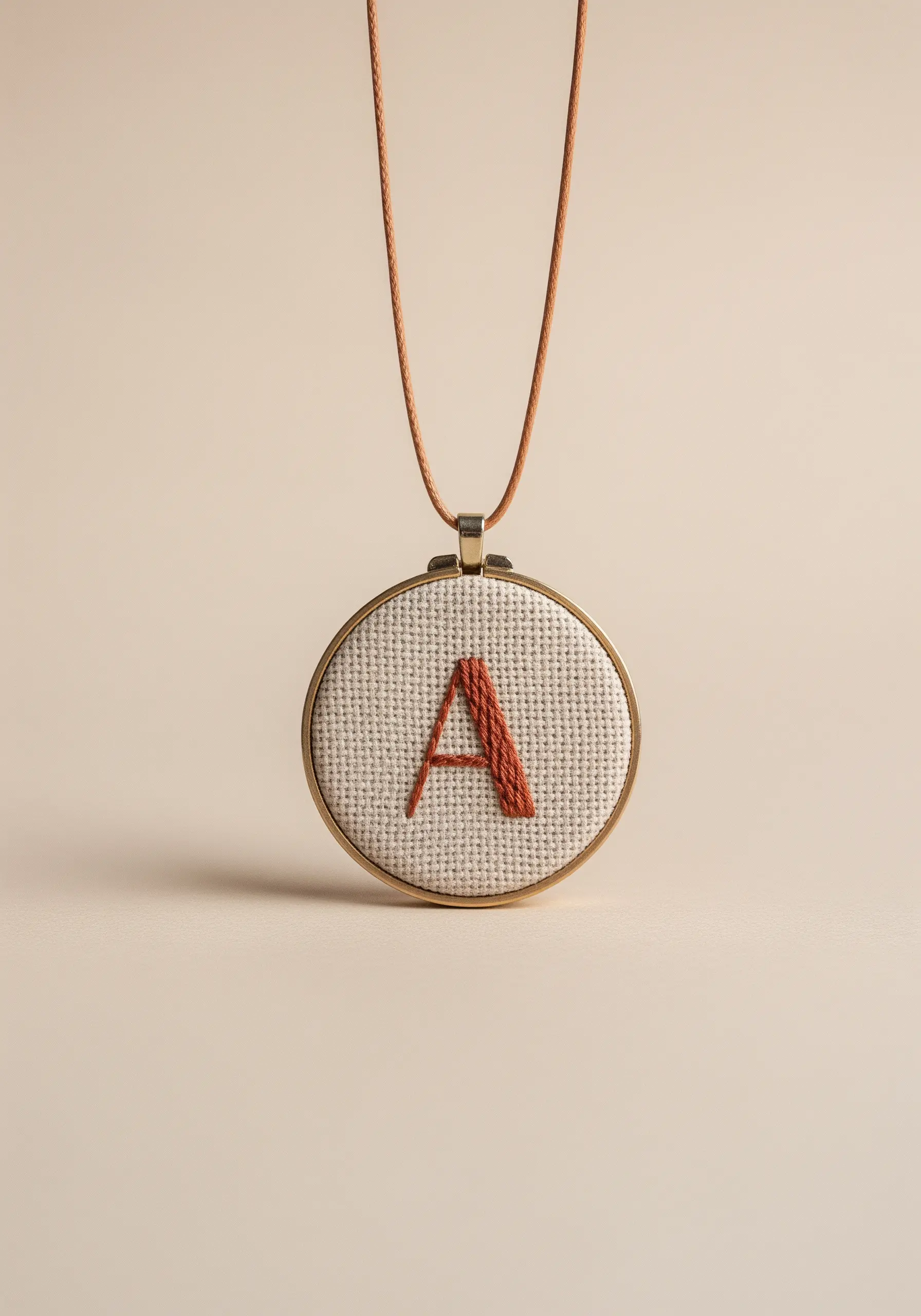 A terracotta-colored initial 'A' embroidered with padded satin stitch in a mini hoop.