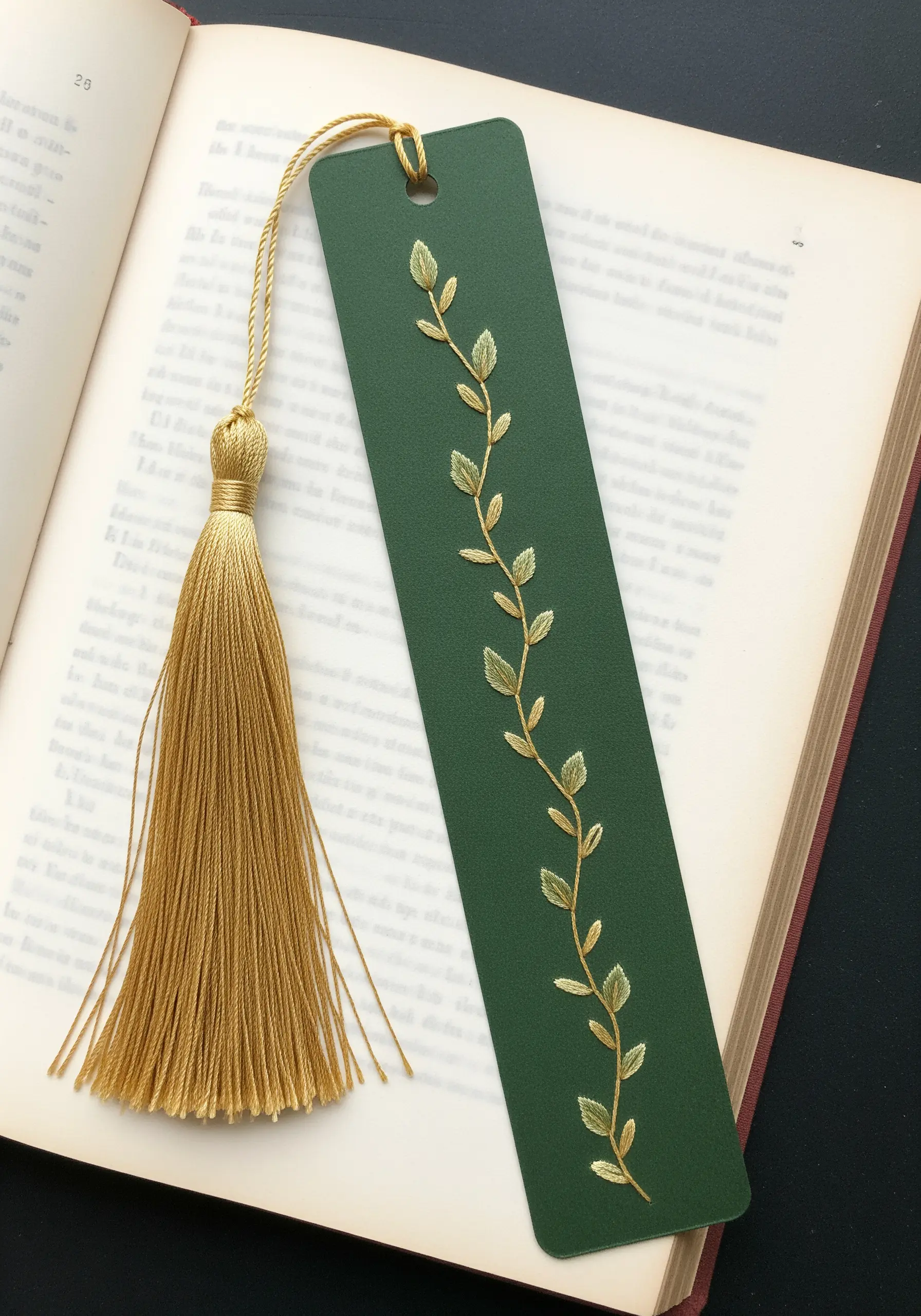 A dark green paper bookmark with a delicate vine embroidered in gold and green thread.