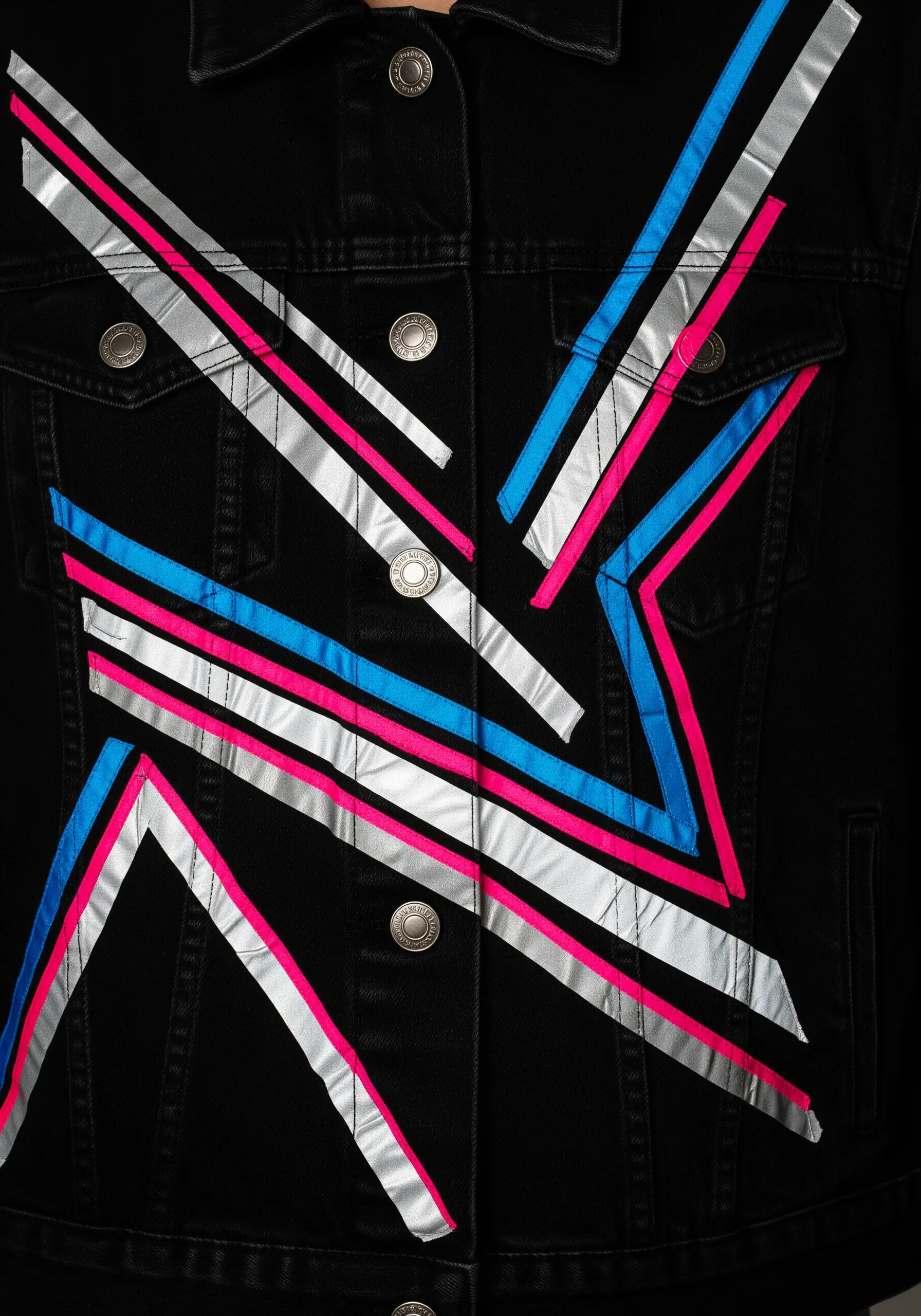 Geometric appliqué on a black denim jacket using silver, pink, and blue ribbon.
