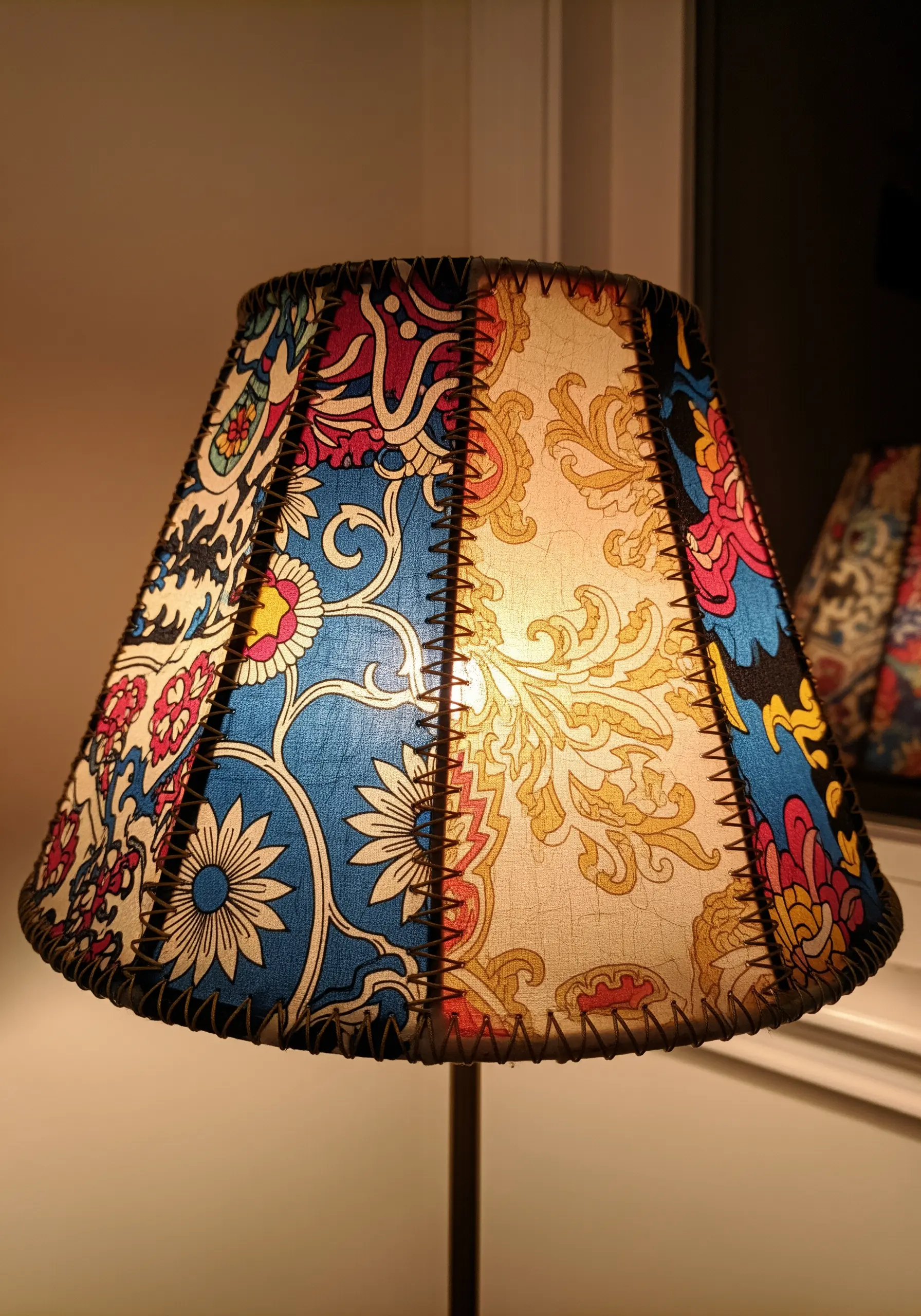 A lampshade covered in colorful patchwork fabric panels joined by dark, visible stitching.