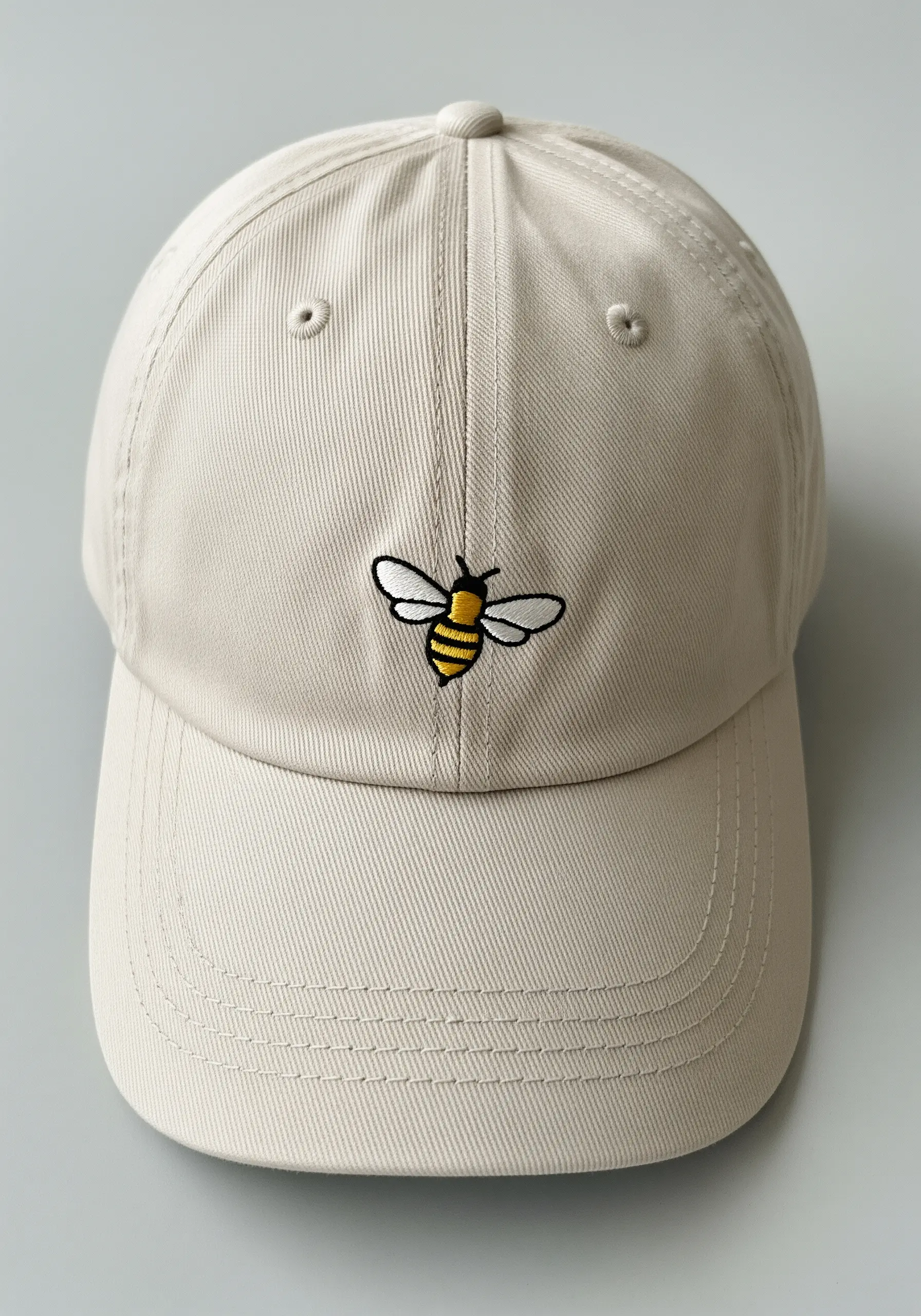 A small embroidered bee with satin stitch body and backstitch wings on a beige baseball cap.