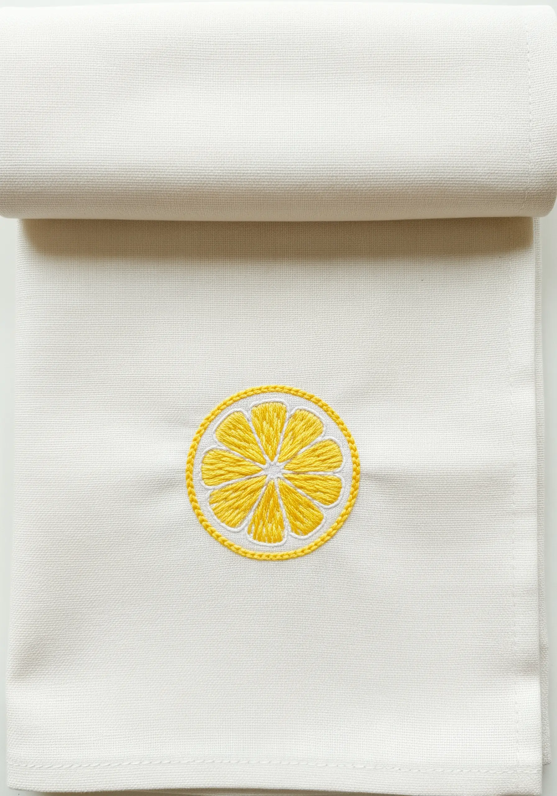 A mini embroidered lemon slice with clean satin stitch segments on a white kitchen towel.