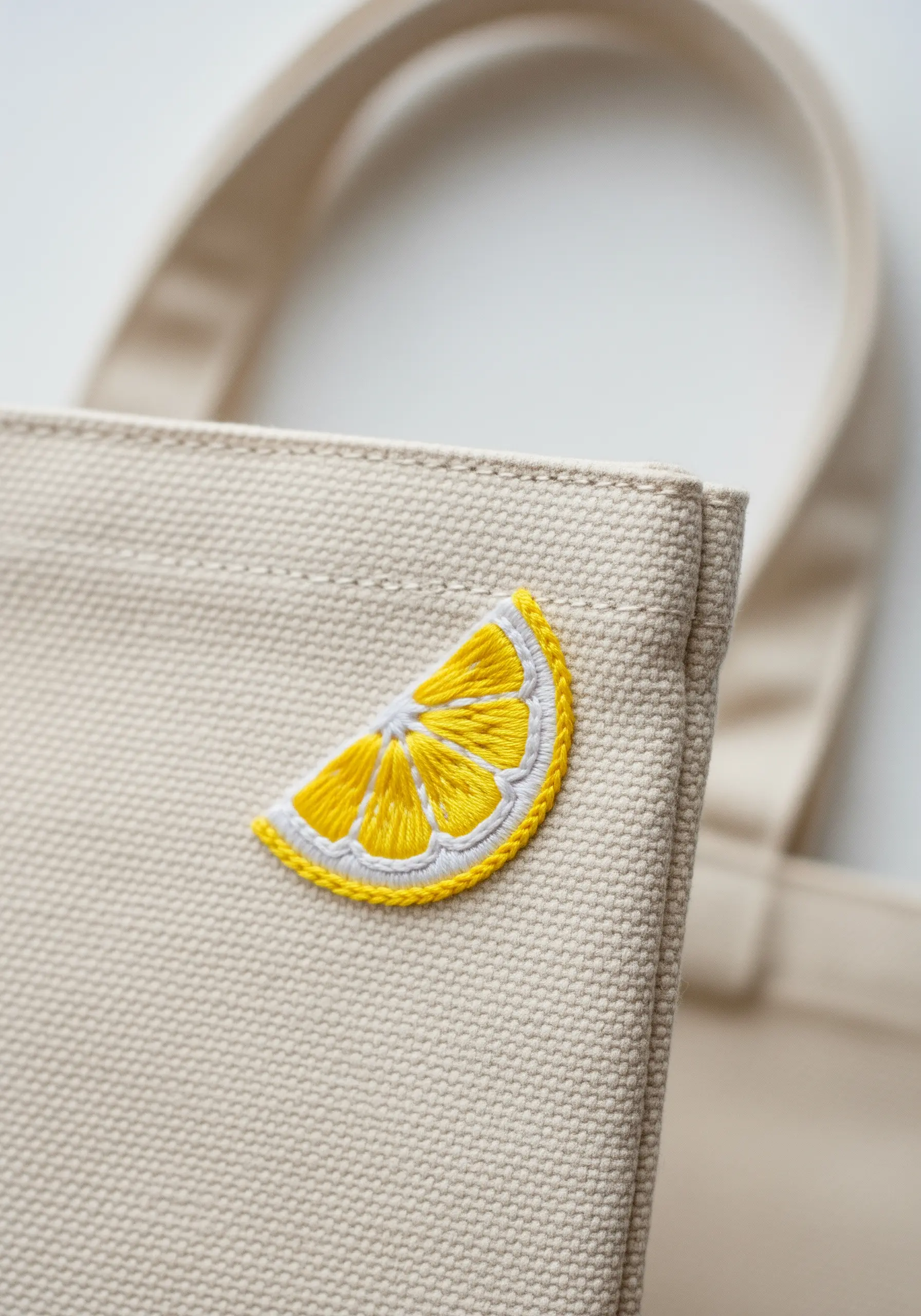 Close-up of a vibrant yellow and white embroidered lemon slice on a canvas tote bag.