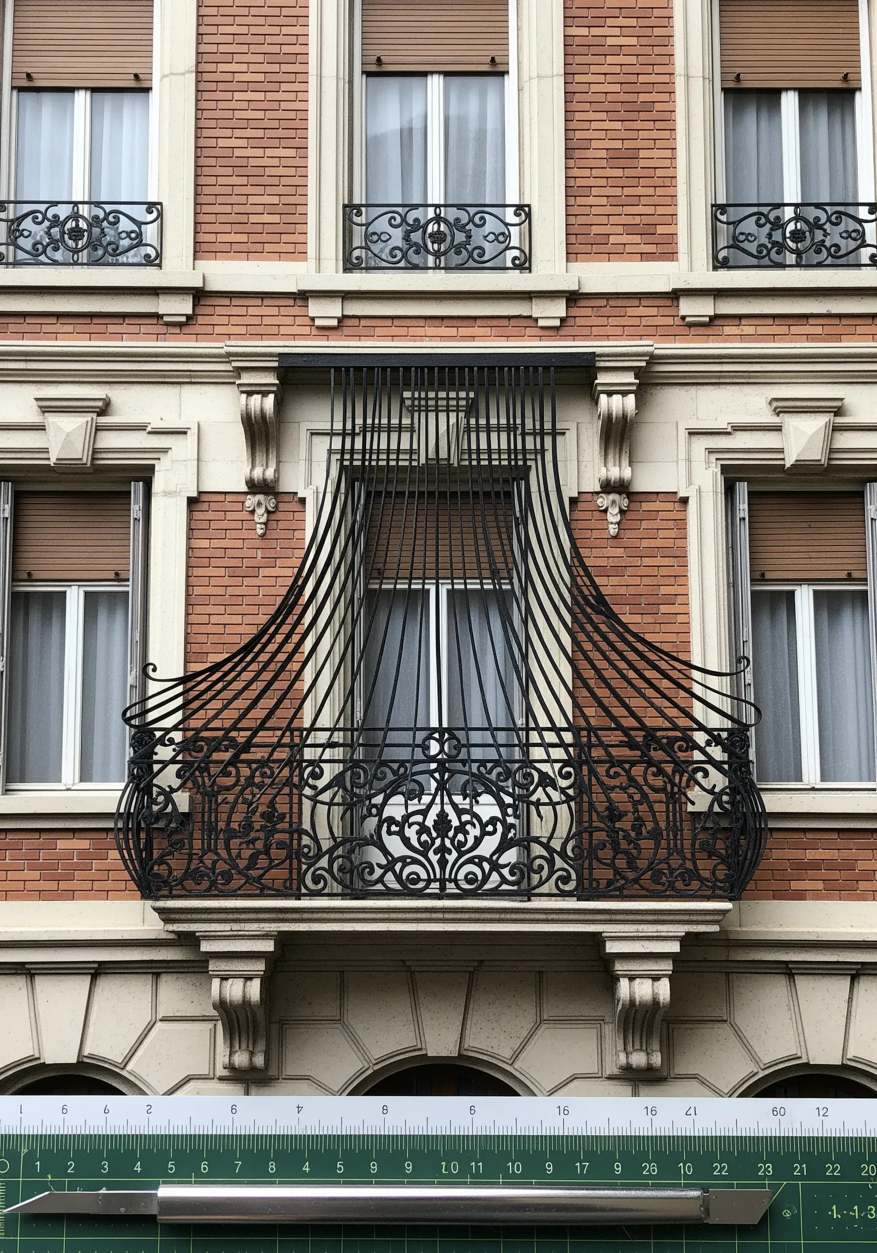 A paper art replica of an ornate wrought iron balcony on a brick building.