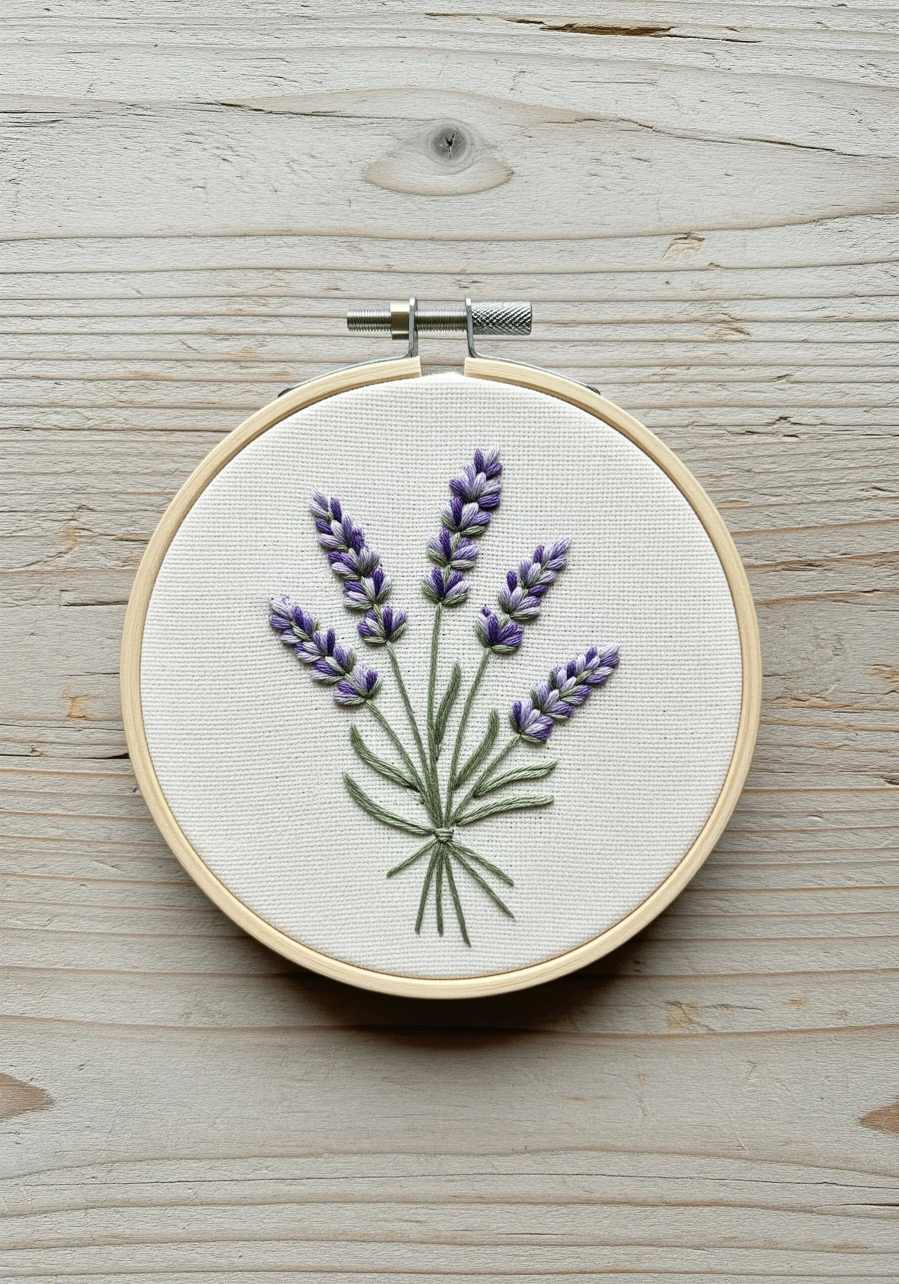 Hand-embroidered lavender bouquet in a small hoop with textured purple florets and green stems.