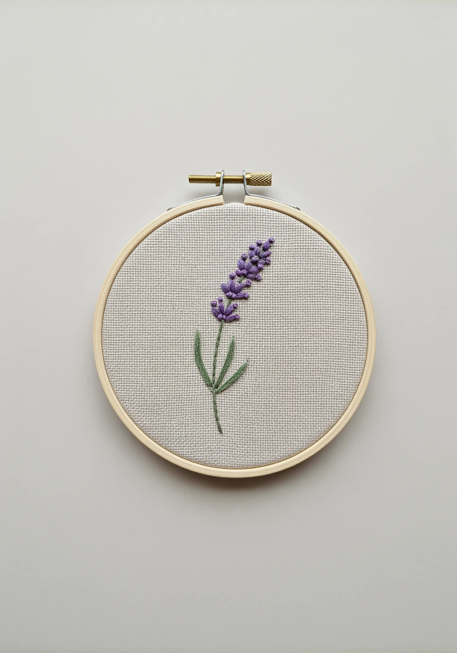 A simple lavender sprig embroidered with French knots and stem stitch in a wooden hoop.