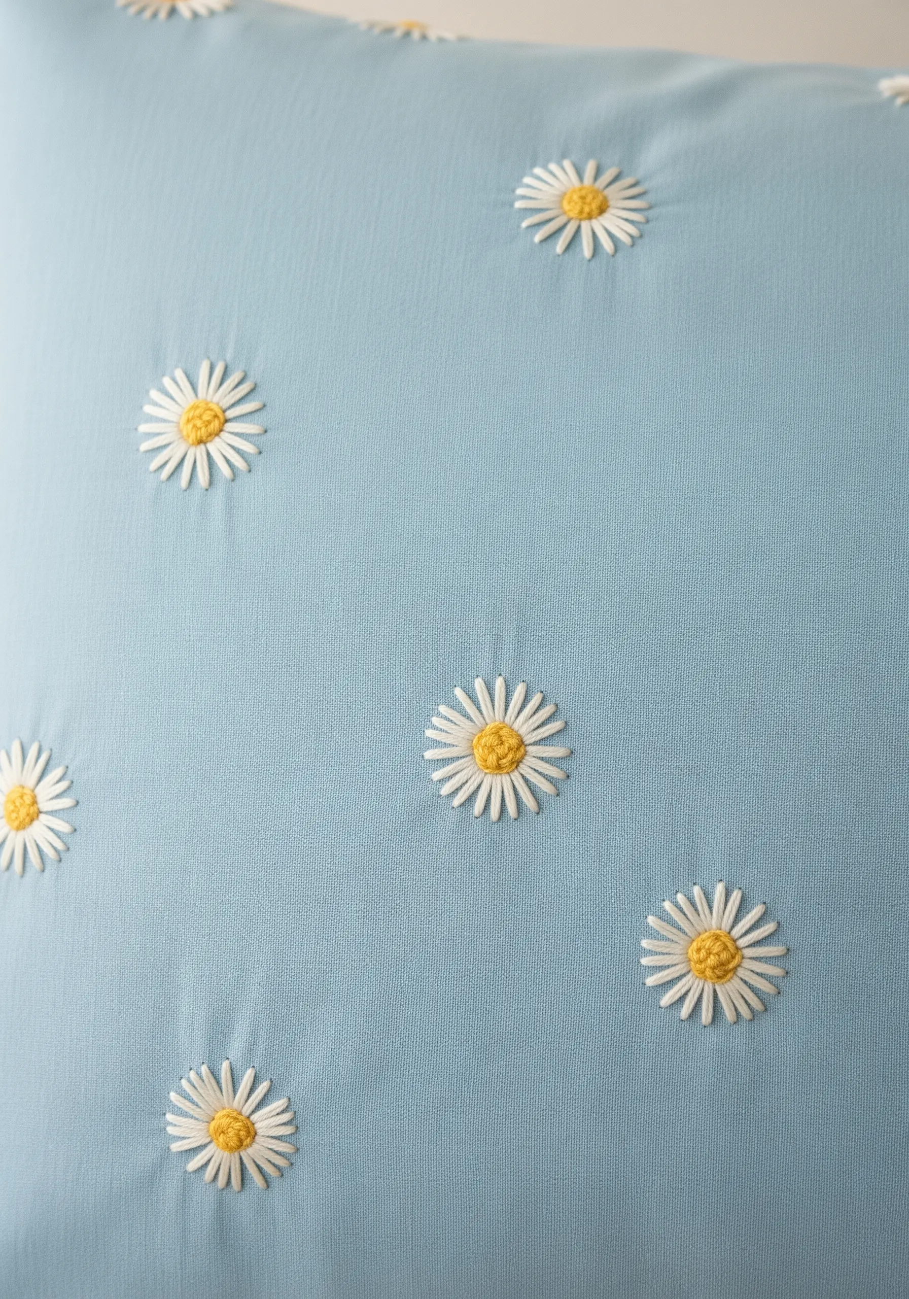 Several small daisies with white petals and yellow centers embroidered on a light blue pillowcase.