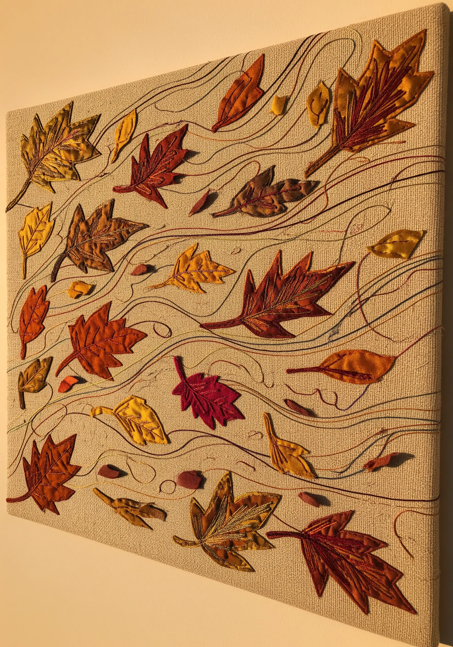 Embroidery on canvas depicting autumn leaves in orange and yellow, scattered by wind.