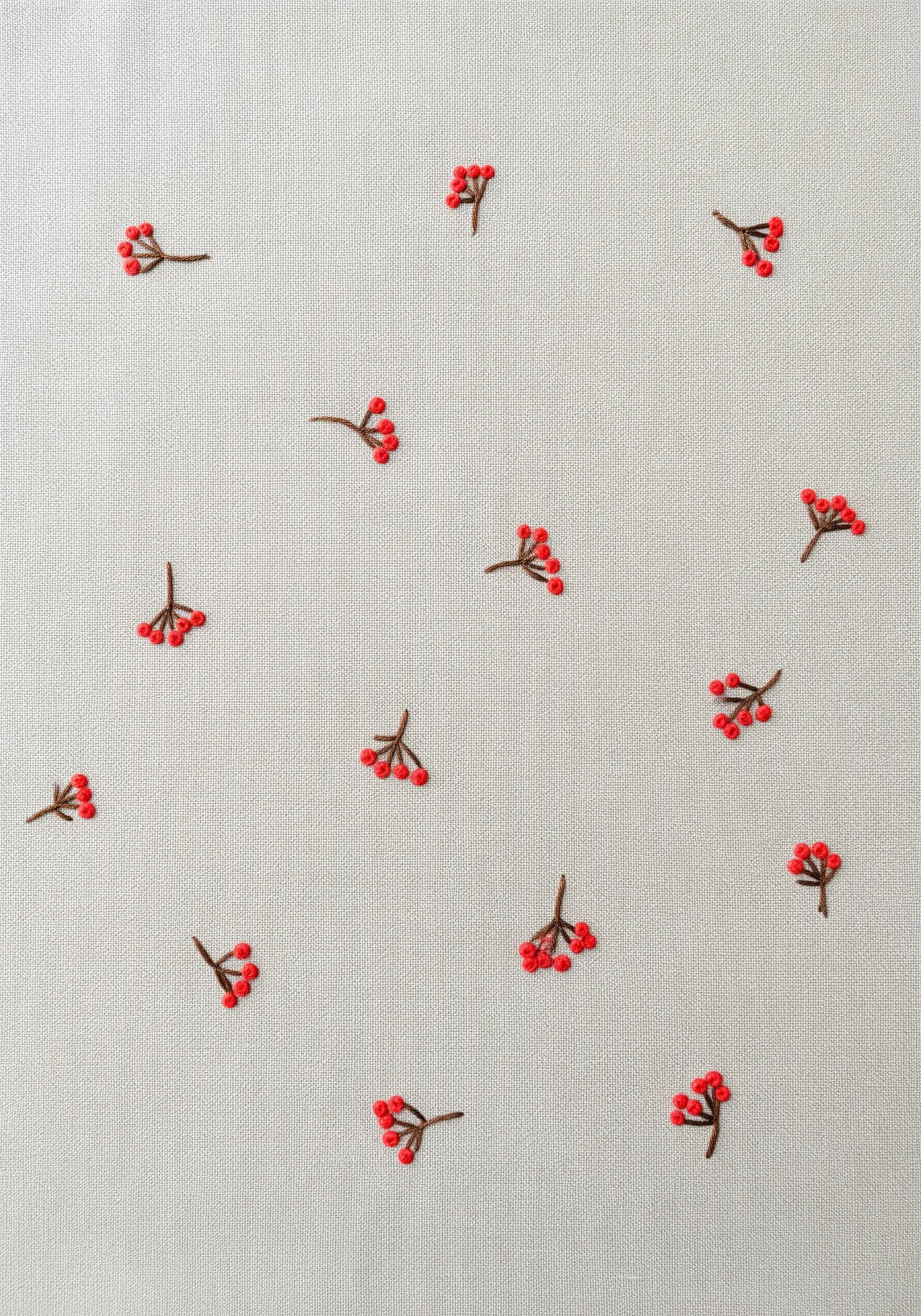 A scatter pattern of tiny red winter berries embroidered on light linen fabric.