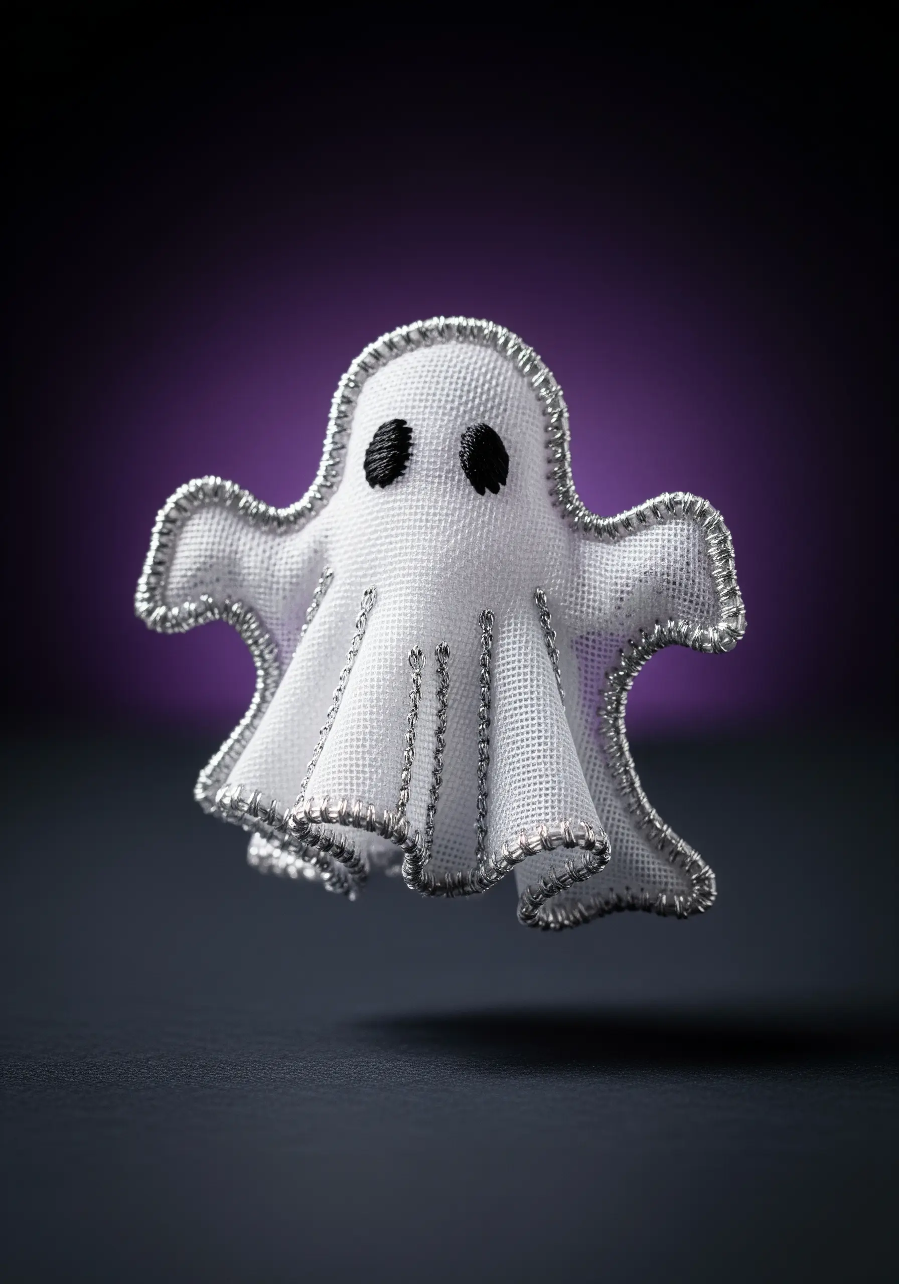 A small, three-dimensional embroidered ghost ornament with silver thread details, appearing to float.