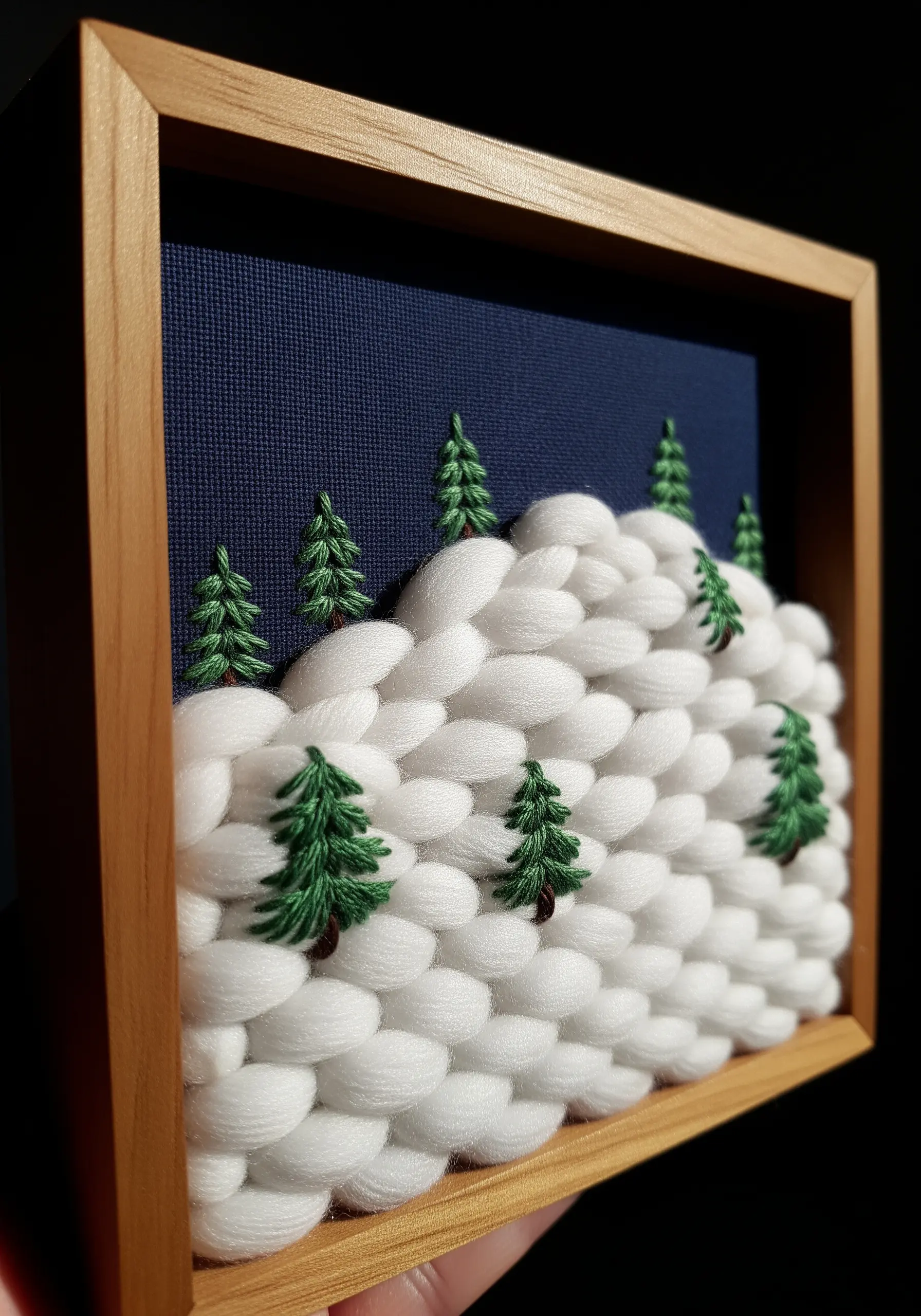 A 3D embroidered winter scene with plush white yarn snowdrifts and small green trees.