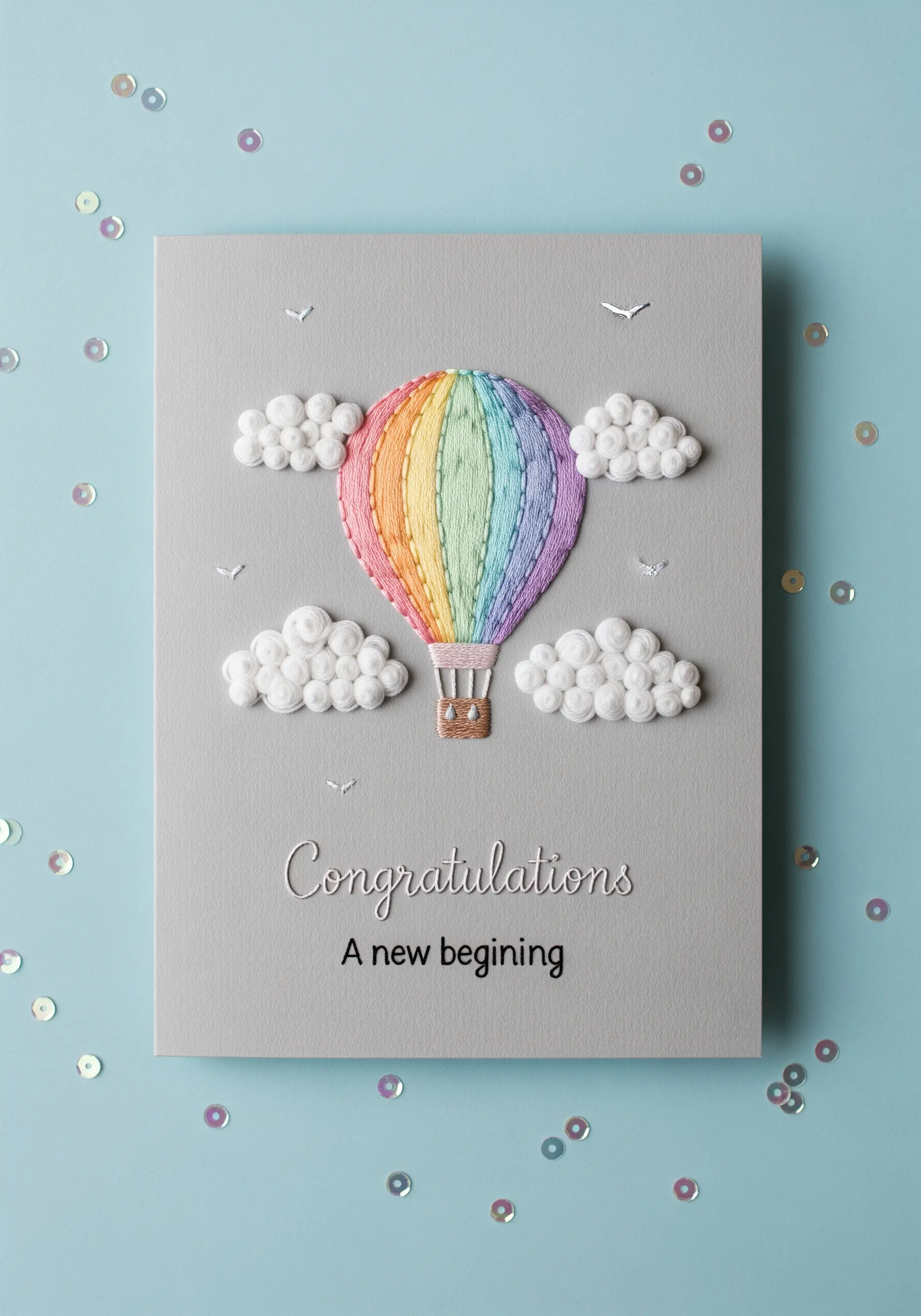 A greeting card with a satin-stitched hot air balloon surrounded by puffy French knot clouds.