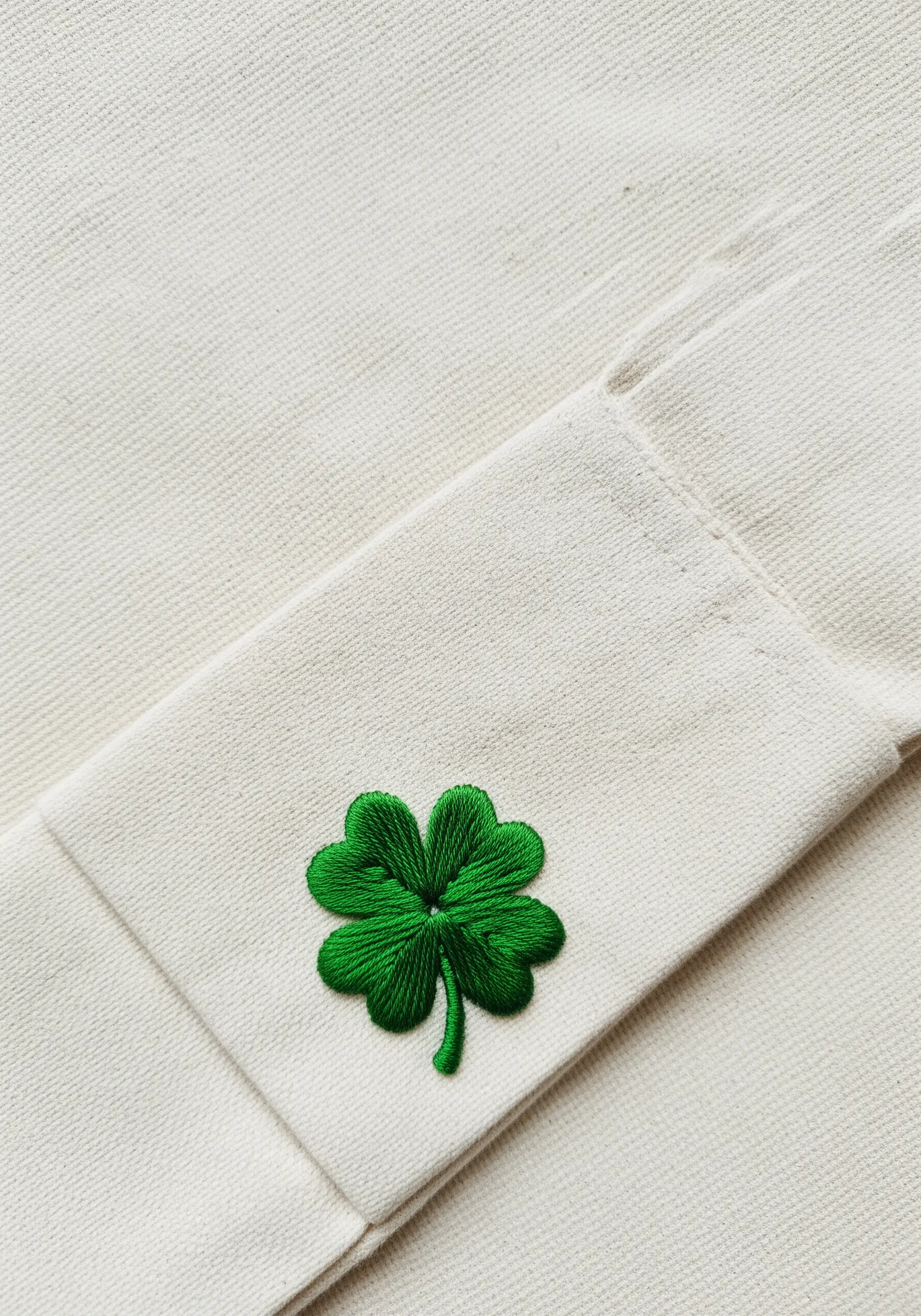 A vibrant green four-leaf clover embroidered on the strap of a canvas tote bag.