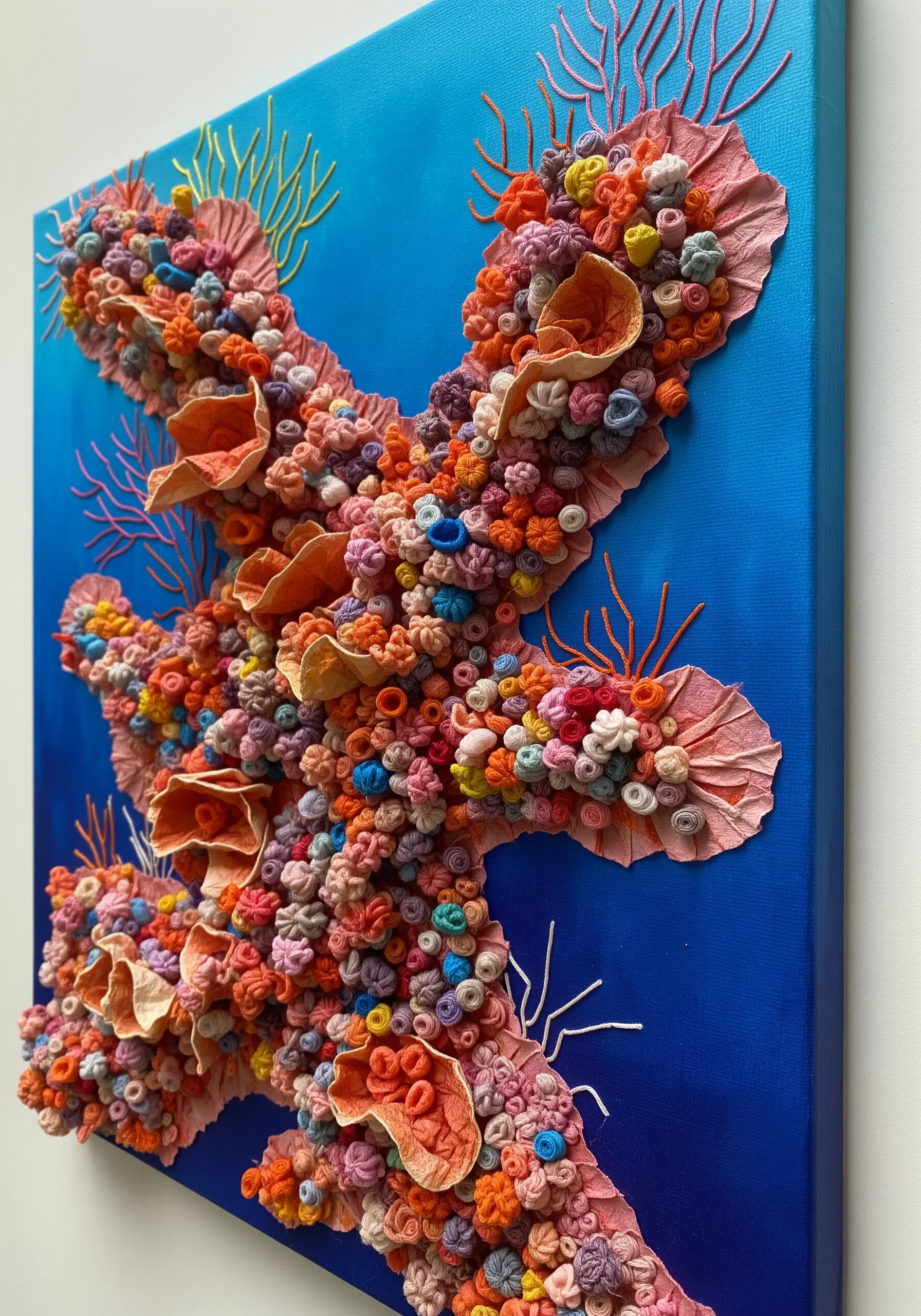 A 3D mixed-media artwork of a coral reef on canvas, using fabric, paper, and various embroidery knots.