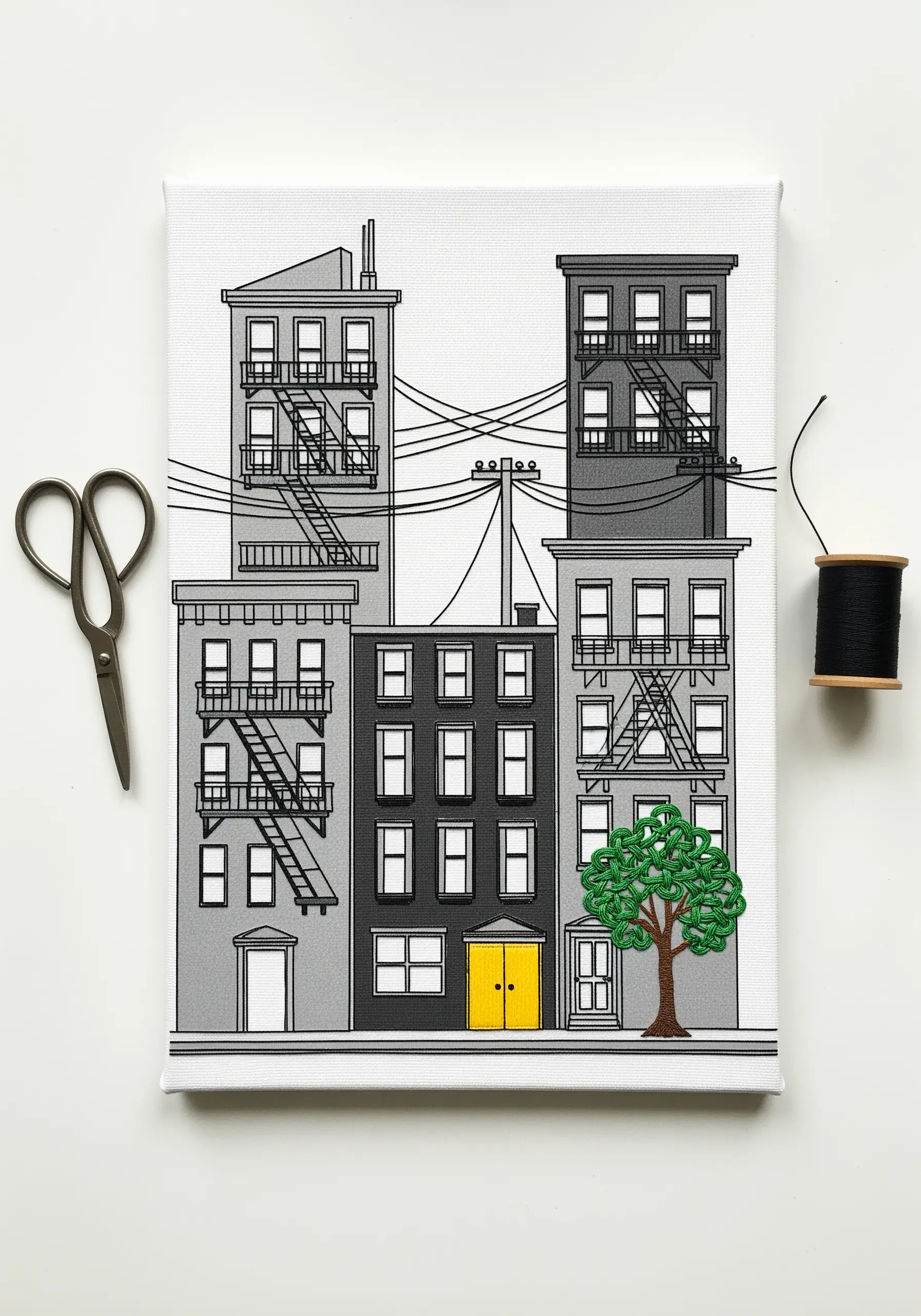 A printed canvas of city buildings where one tree is filled with green embroidery stitches.