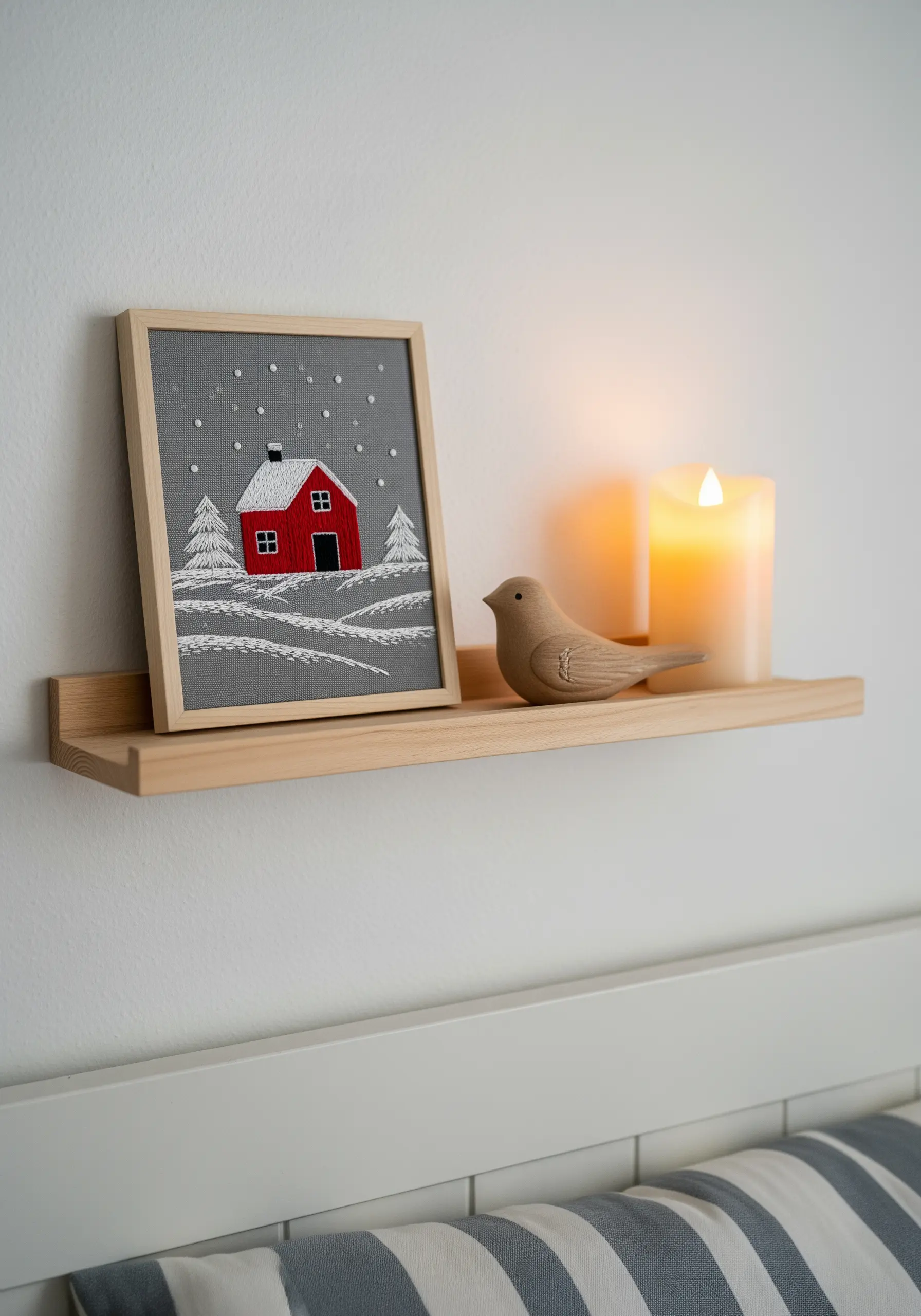 A winter scene with a red cabin embroidered on grey fabric that acts as the sky.