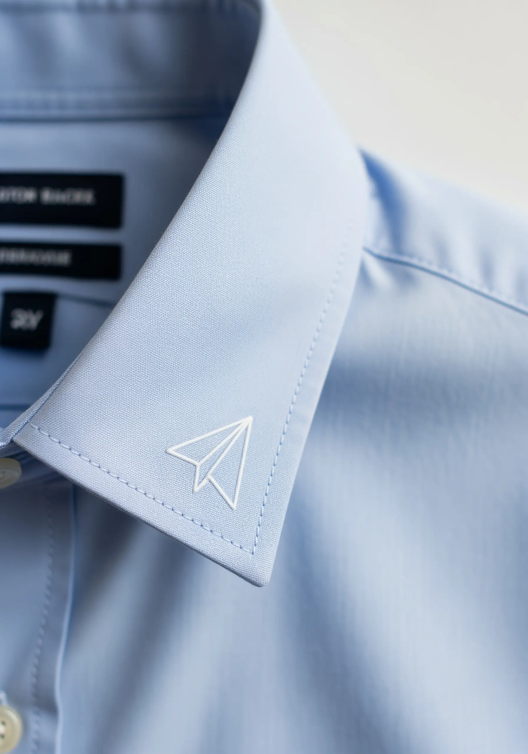 Minimalist white paper airplane outline embroidered on a blue shirt collar.