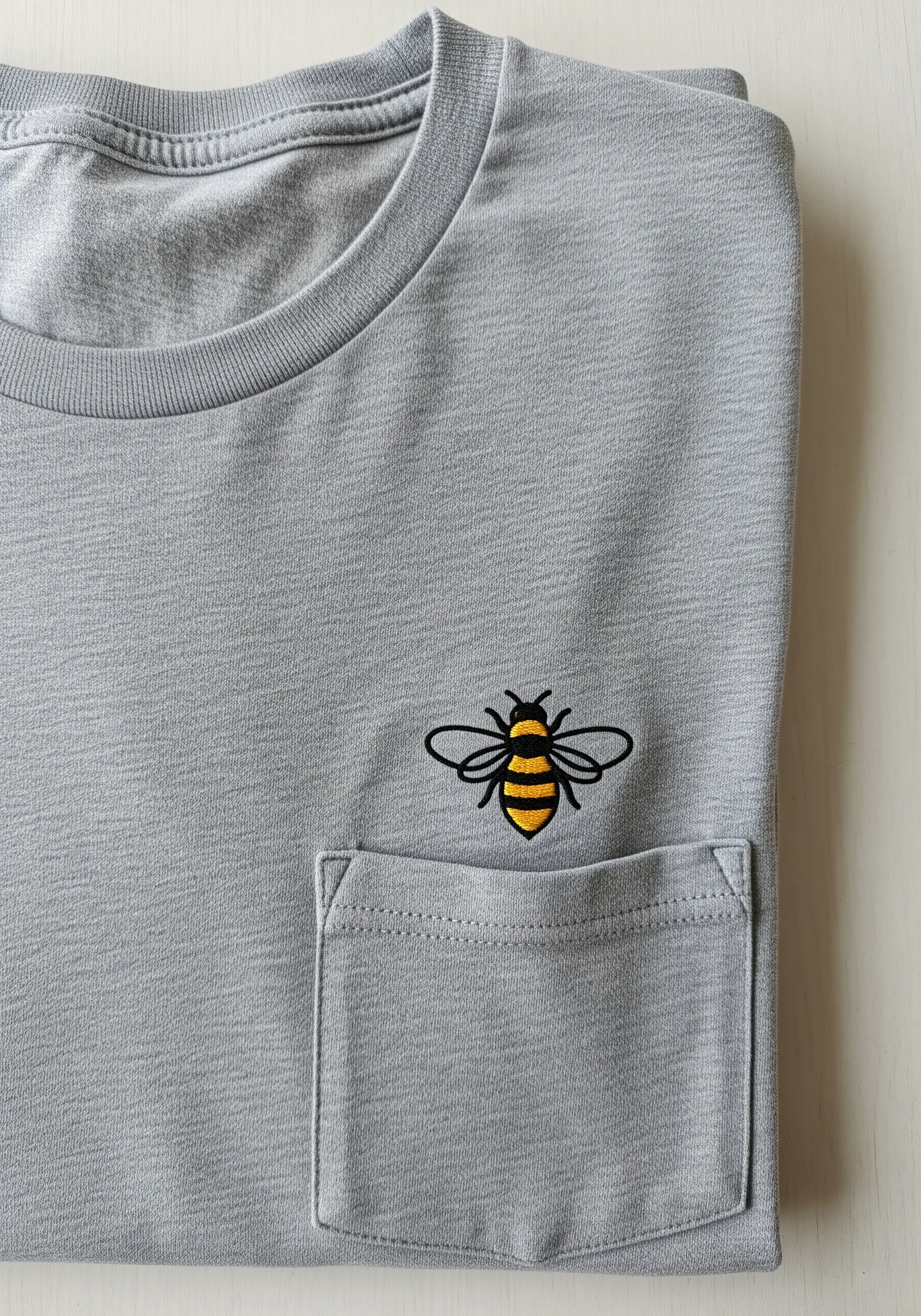 A small, graphic bee with clean black outlines embroidered above a t-shirt pocket.