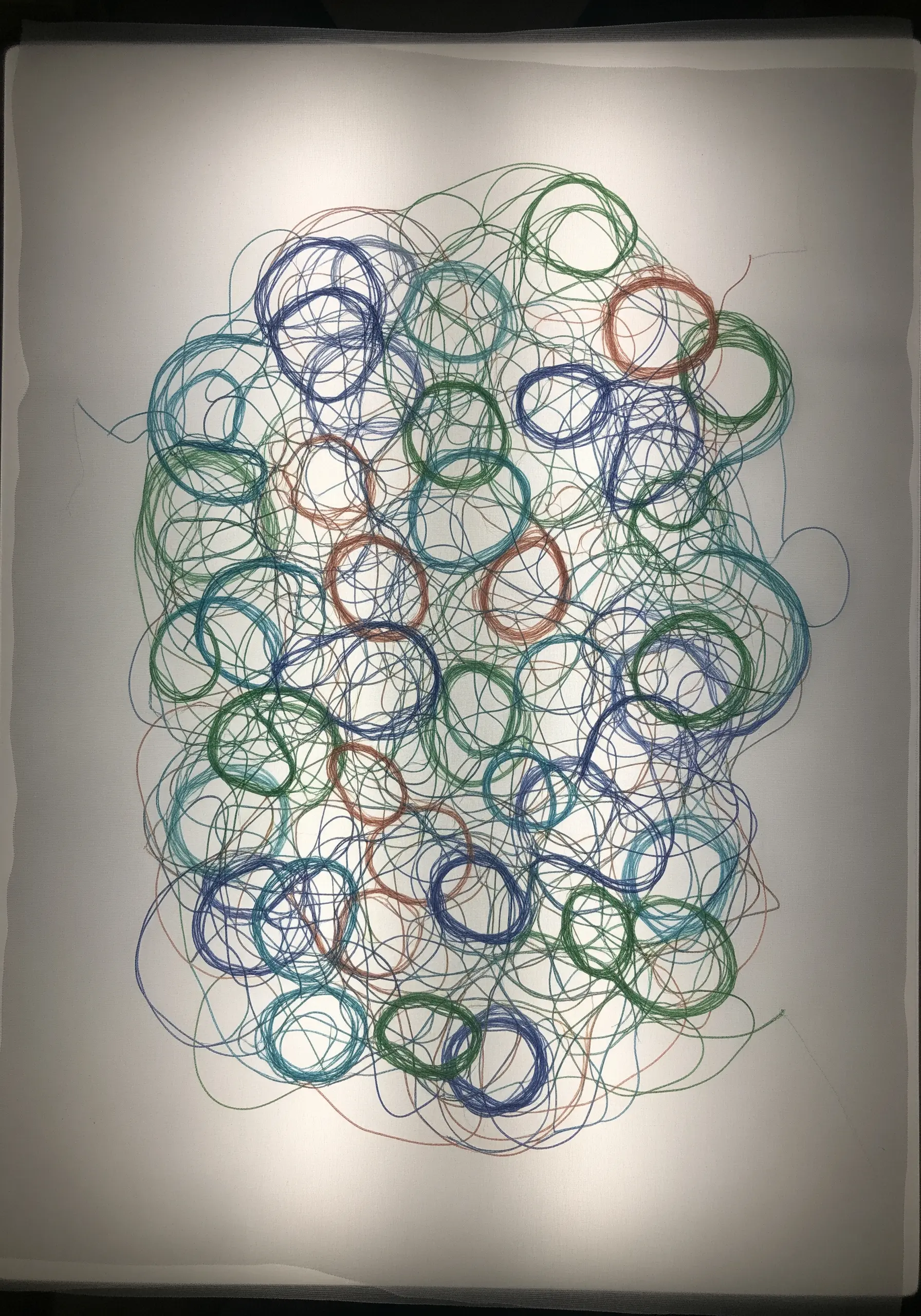Delicate, overlapping thread loops in blue, green, and orange, backlit to appear weightless