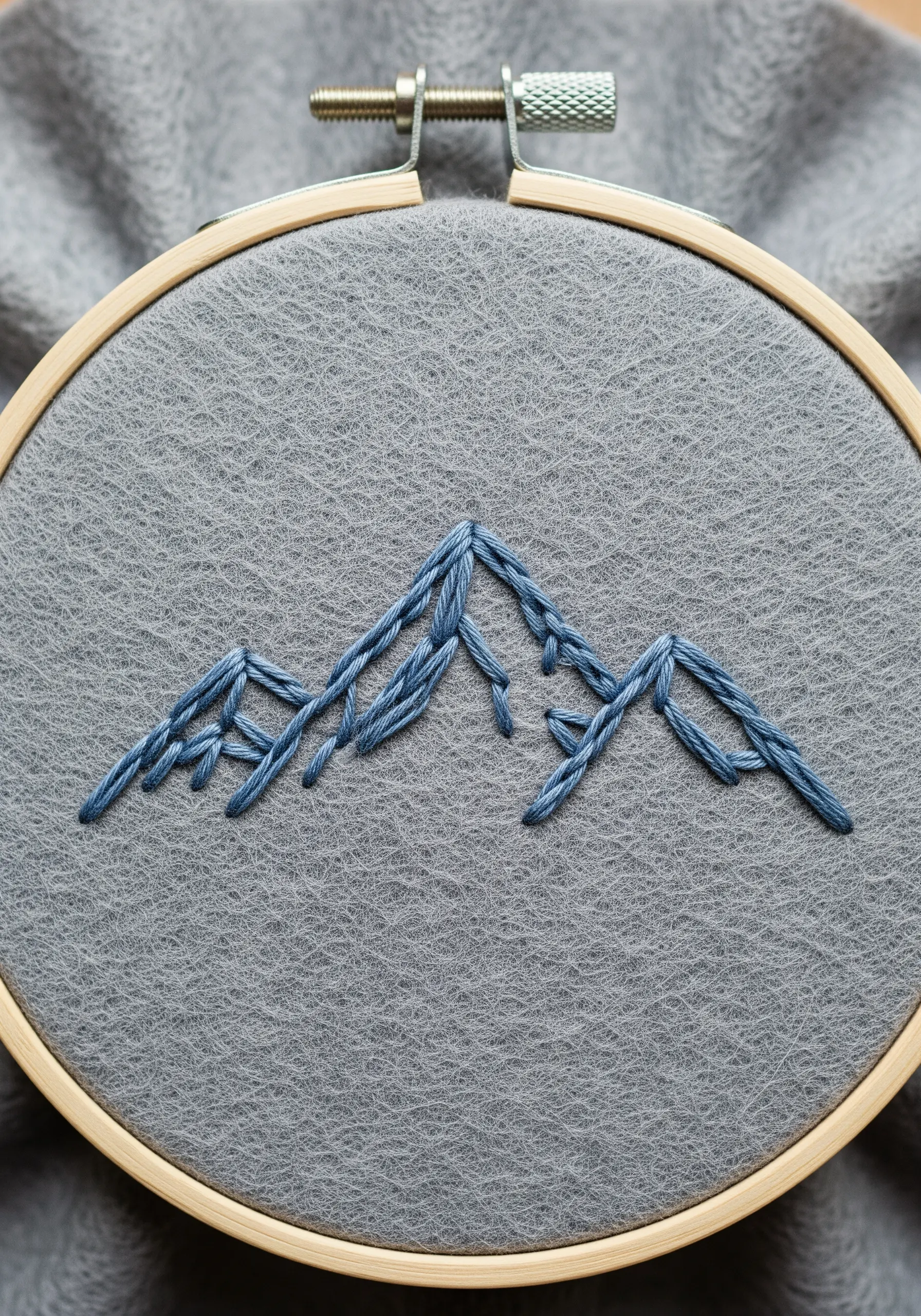 A minimalist mountain range stitched in blue on gray felt.