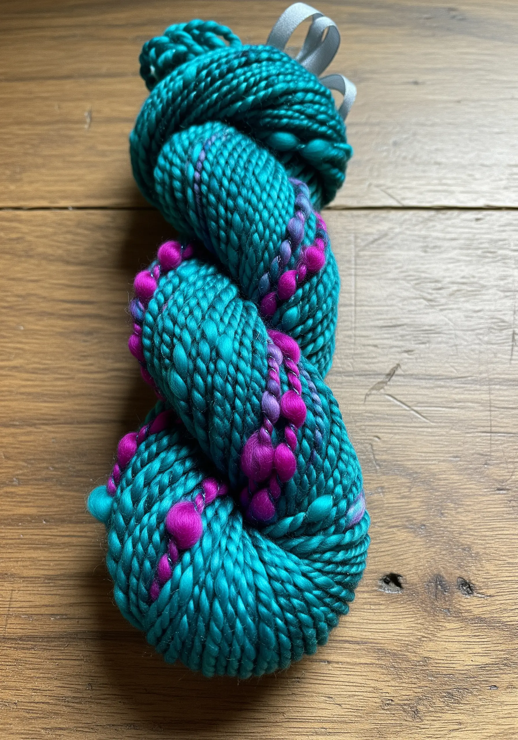 A skein of hand-spun art yarn in a vibrant turquoise with bright pink textured nubs.