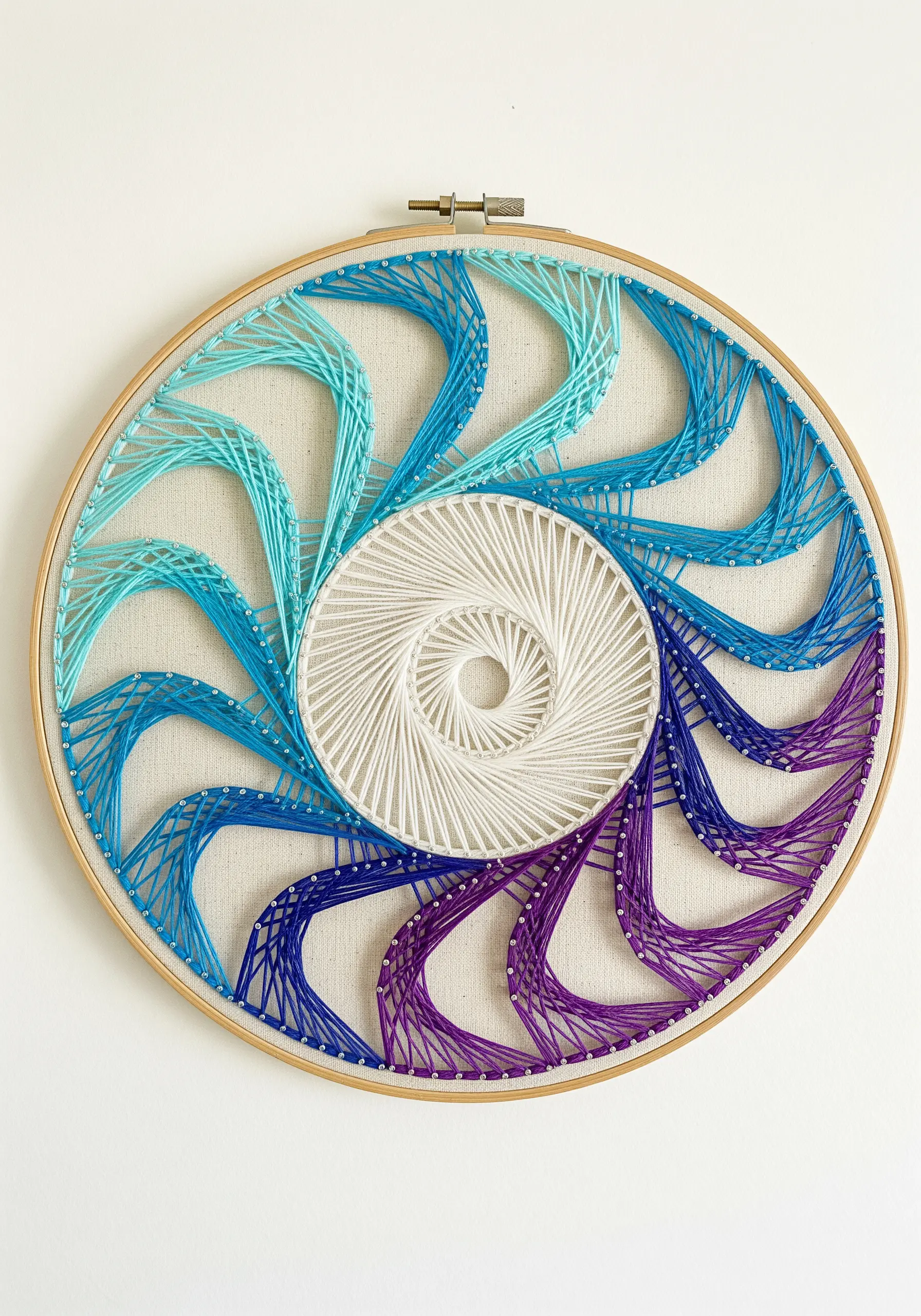 A spiral embroidery hoop with a color gradient from white to purple, creating curved shapes.