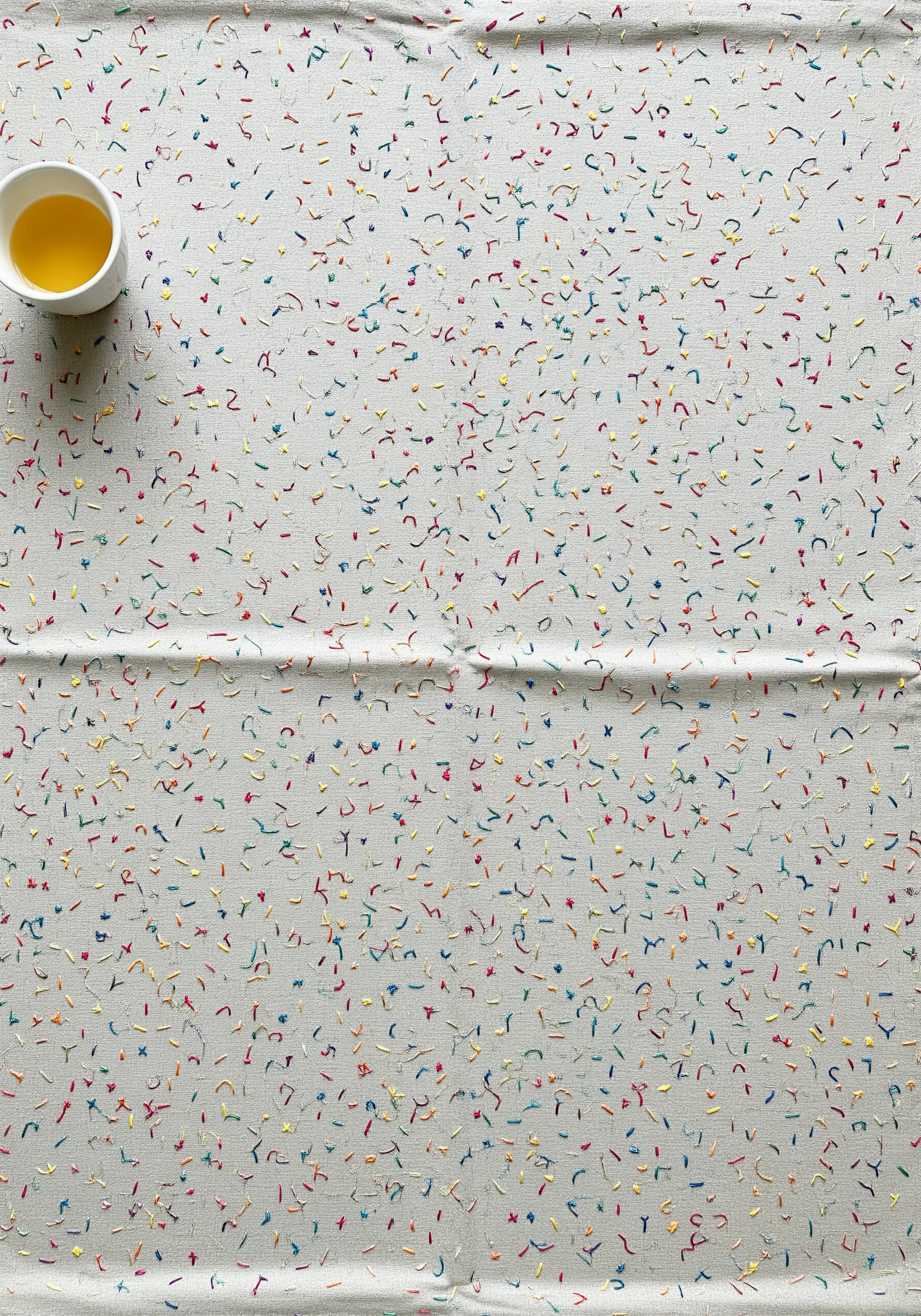 A tablecloth covered in tiny, scattered, random stitches in a rainbow of colors.