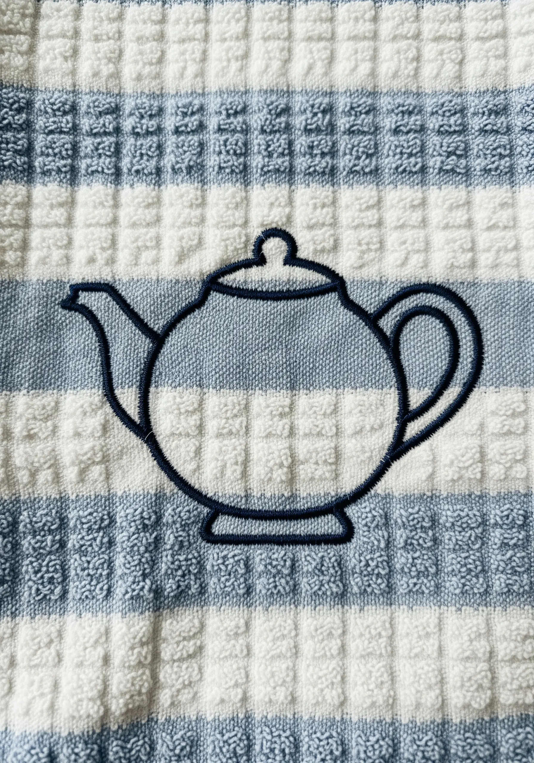A simple teapot outline stitched in dark blue on a blue and white striped terrycloth towel.