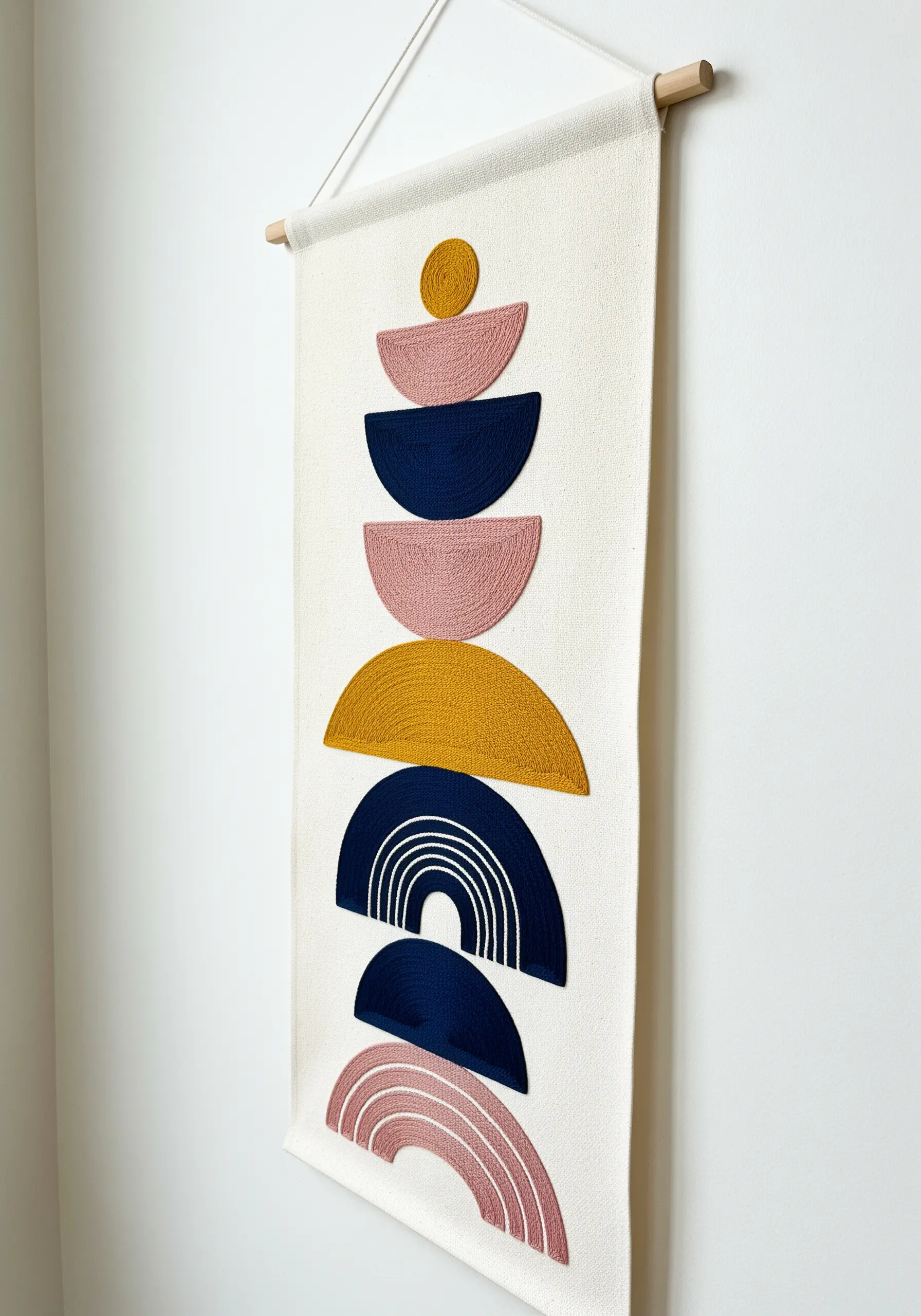 A modern wall hanging with stacked, textured semi-circles in pink, blue, and yellow.