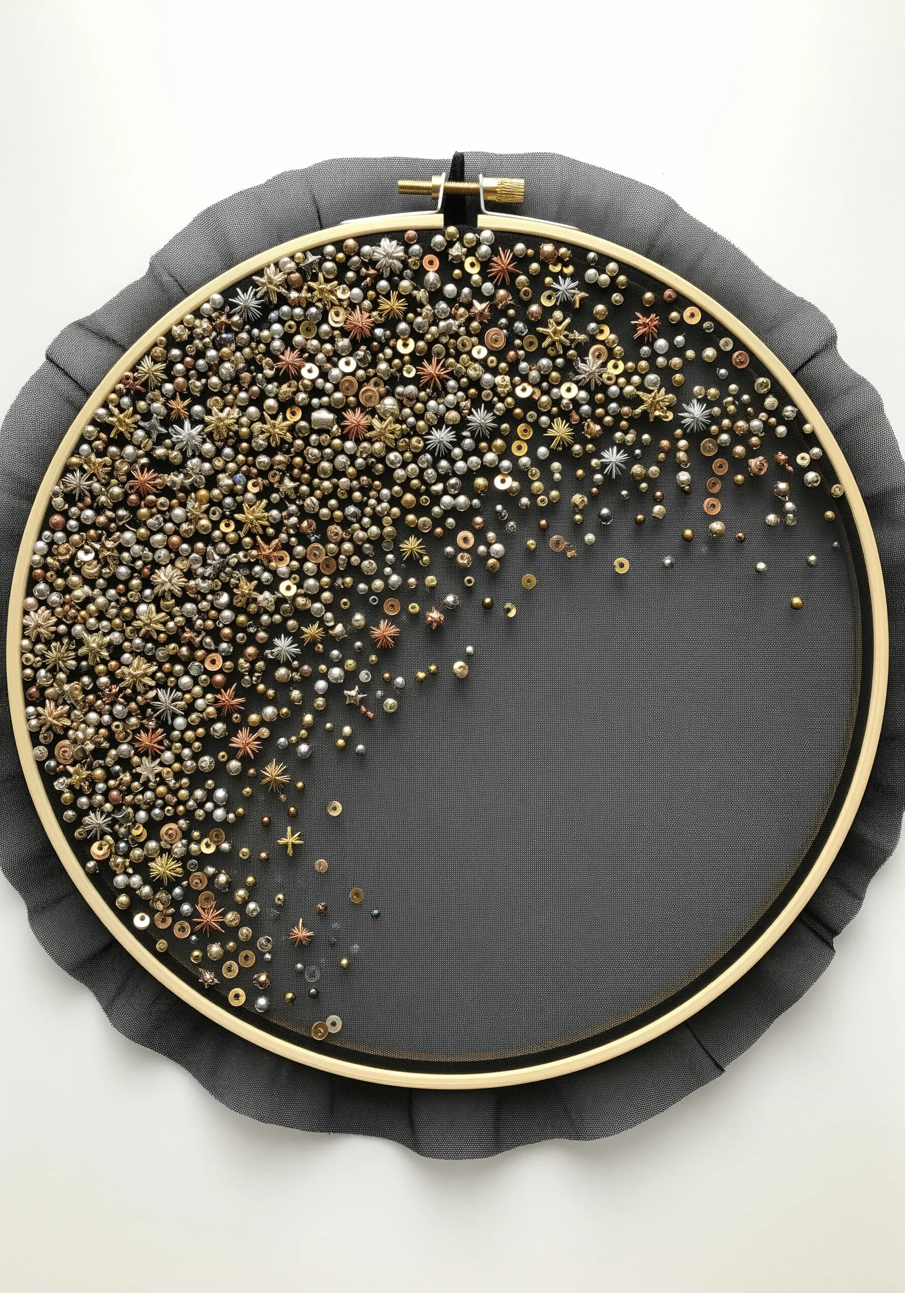 A dense cluster of metallic beads and star sequins stitched onto sheer black tulle in a hoop.