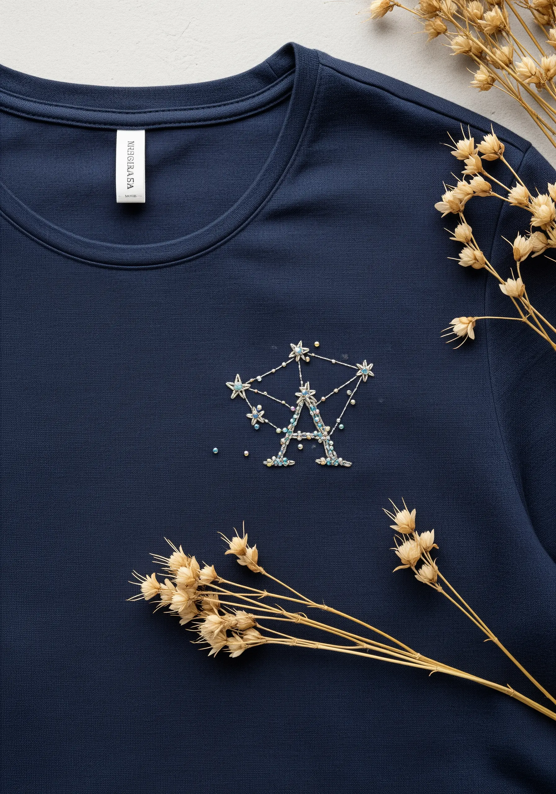 Letter 'A' embroidered to look like a celestial constellation with beads and stars on a navy shirt.
