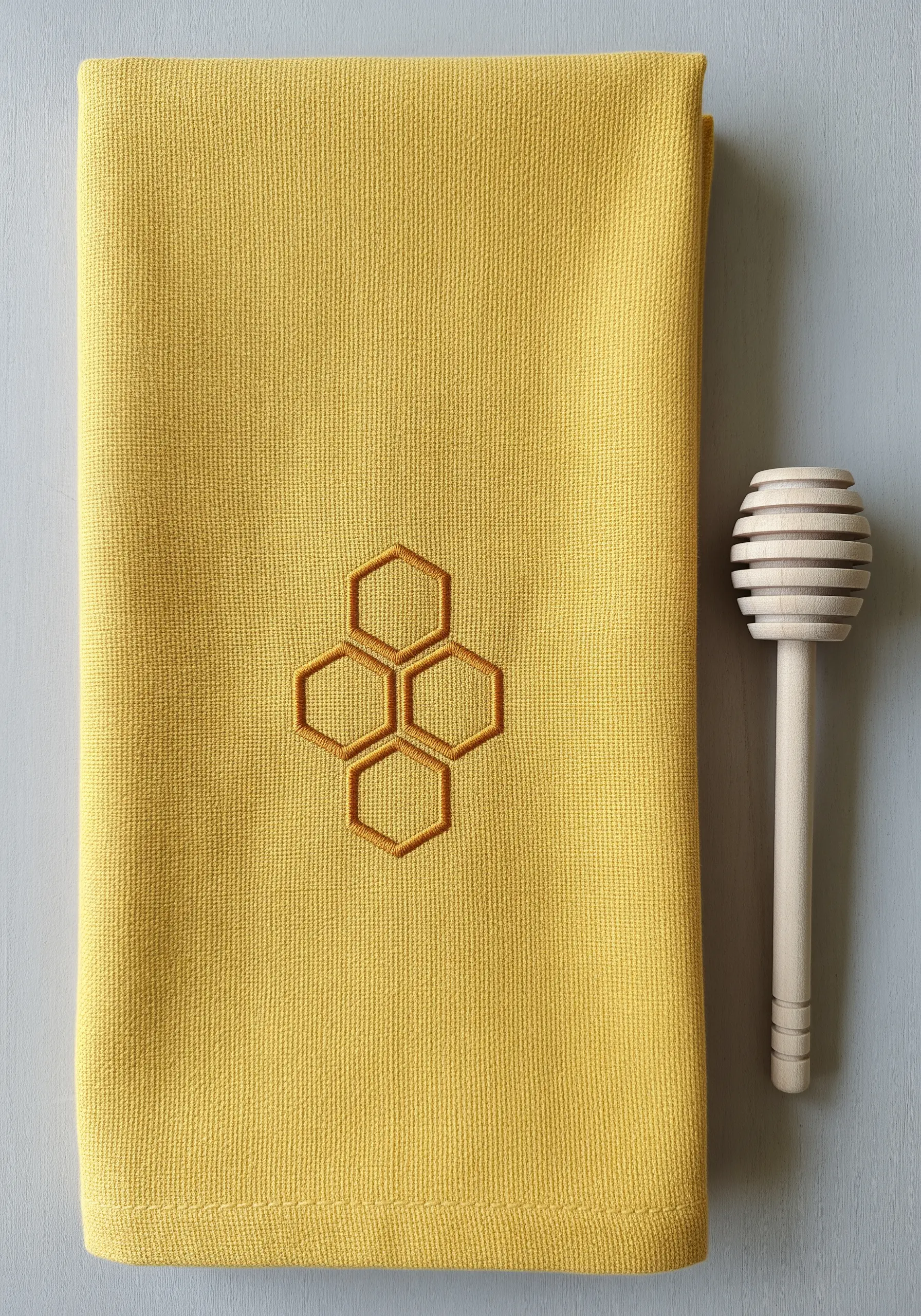 A minimalist honeycomb pattern embroidered in gold thread on a mustard yellow towel.