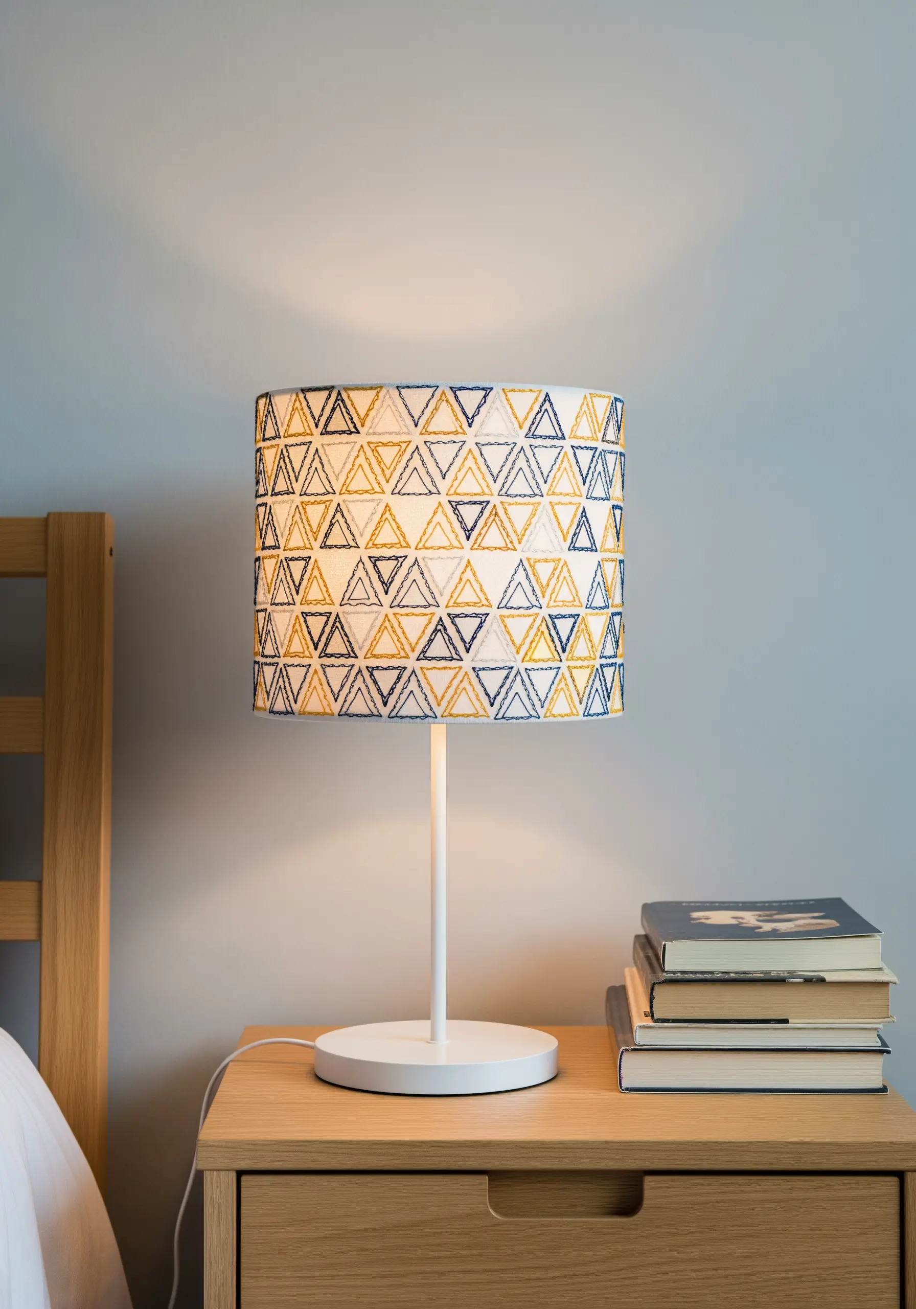 A lampshade covered in fabric embroidered with a repeating pattern of yellow and blue triangles.