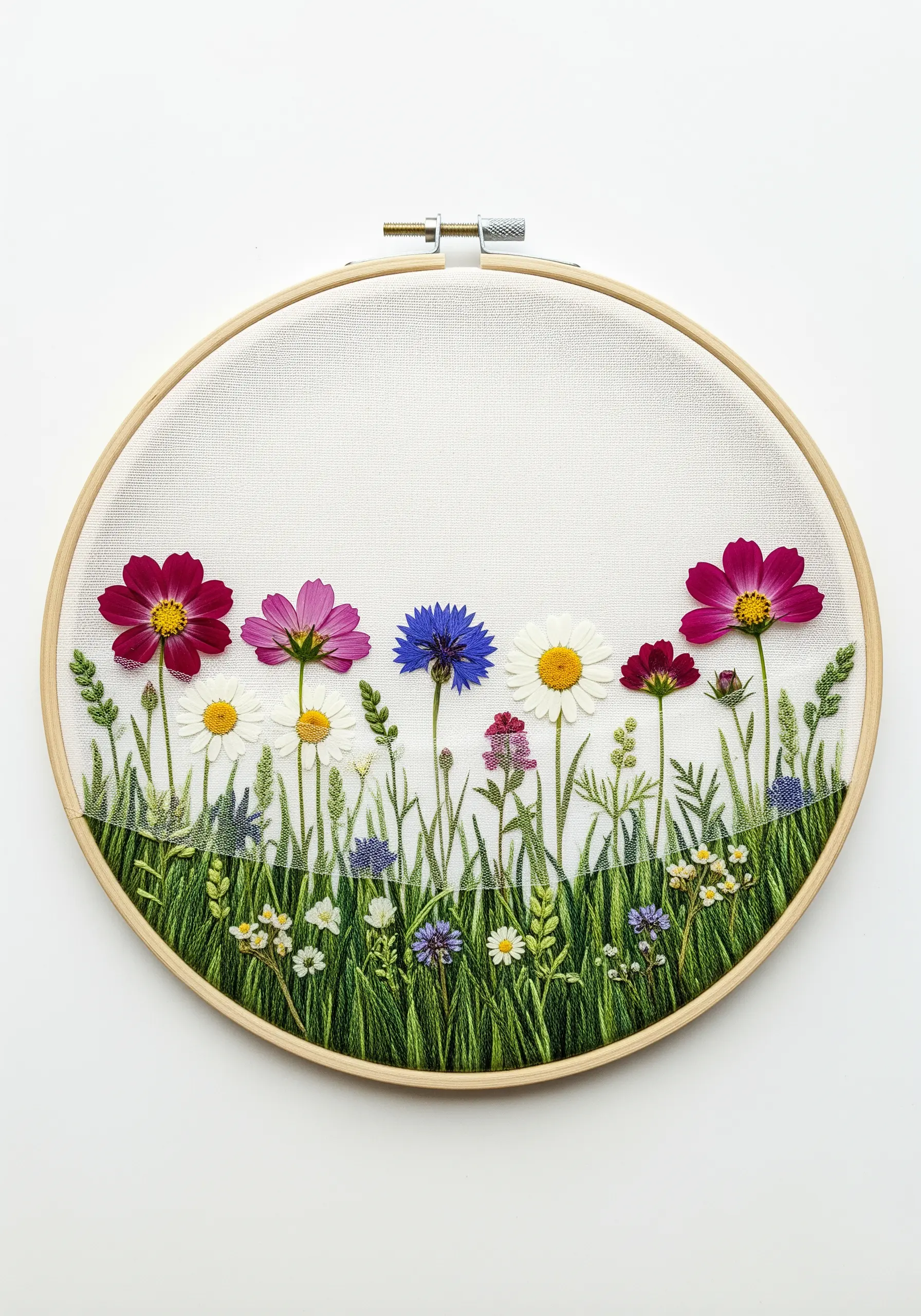 An embroidered field of grass from which real pressed cosmos and daisy flowers are growing.