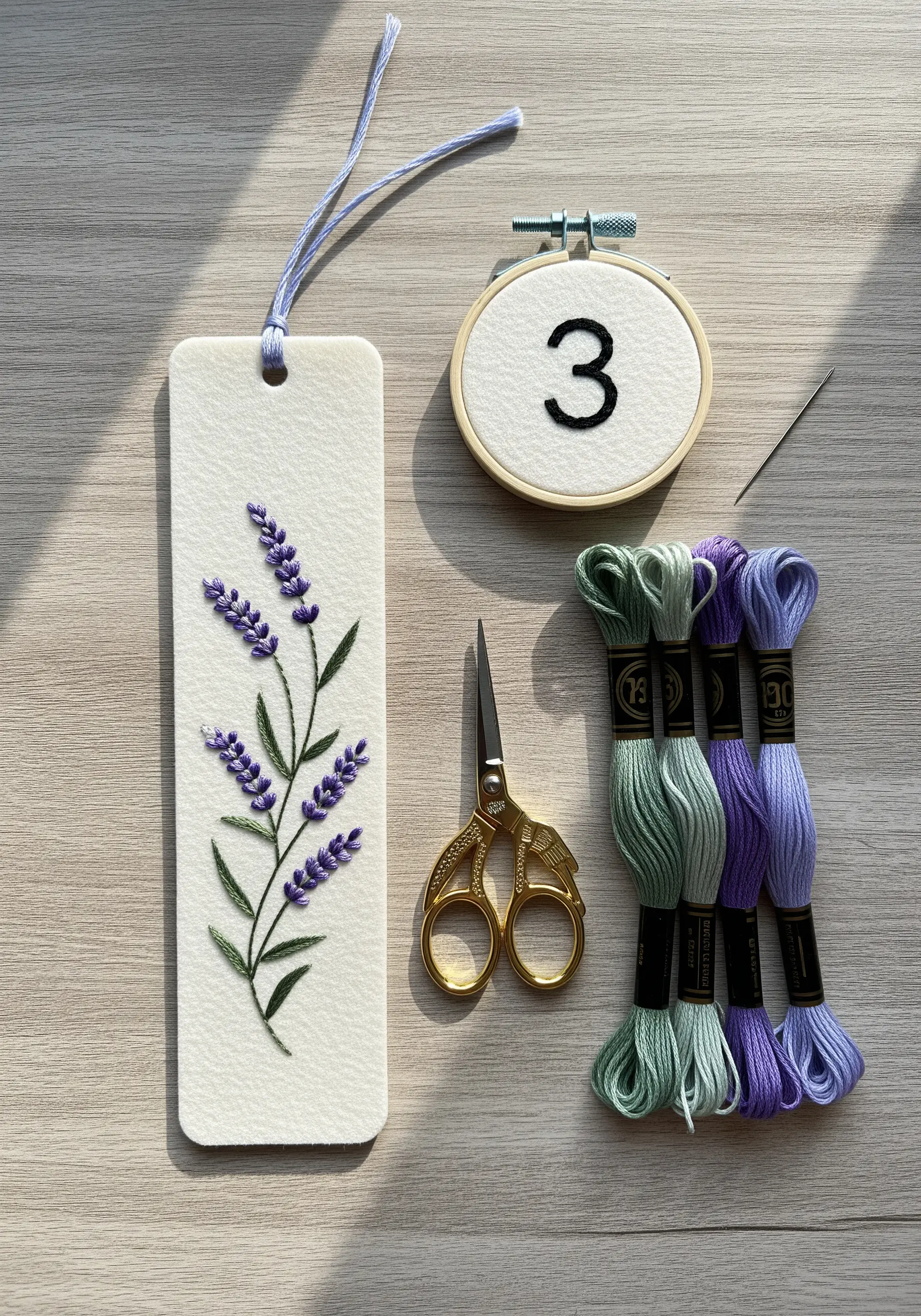 Hand-embroidered lavender sprig on a white paper bookmark with threads and a mini hoop nearby.