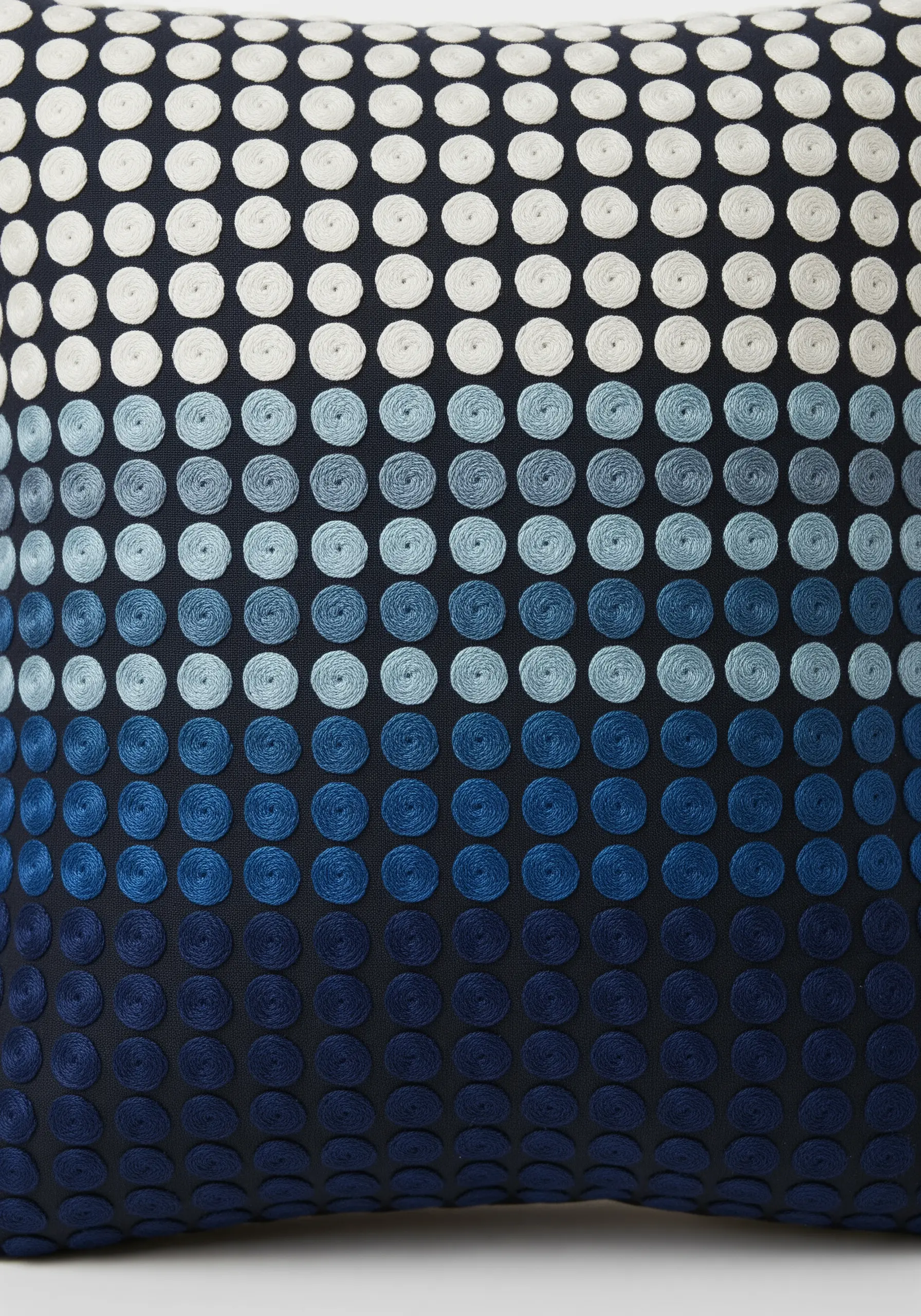 A dark navy pillow covered in a grid of stitched dots that fade from white to deep blue.