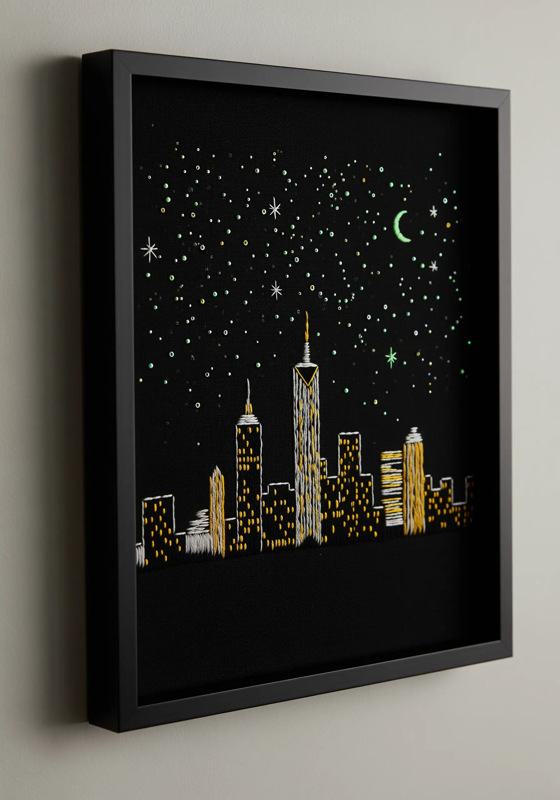 An embroidered city skyline at night on black fabric, using yellow and white thread for lights.