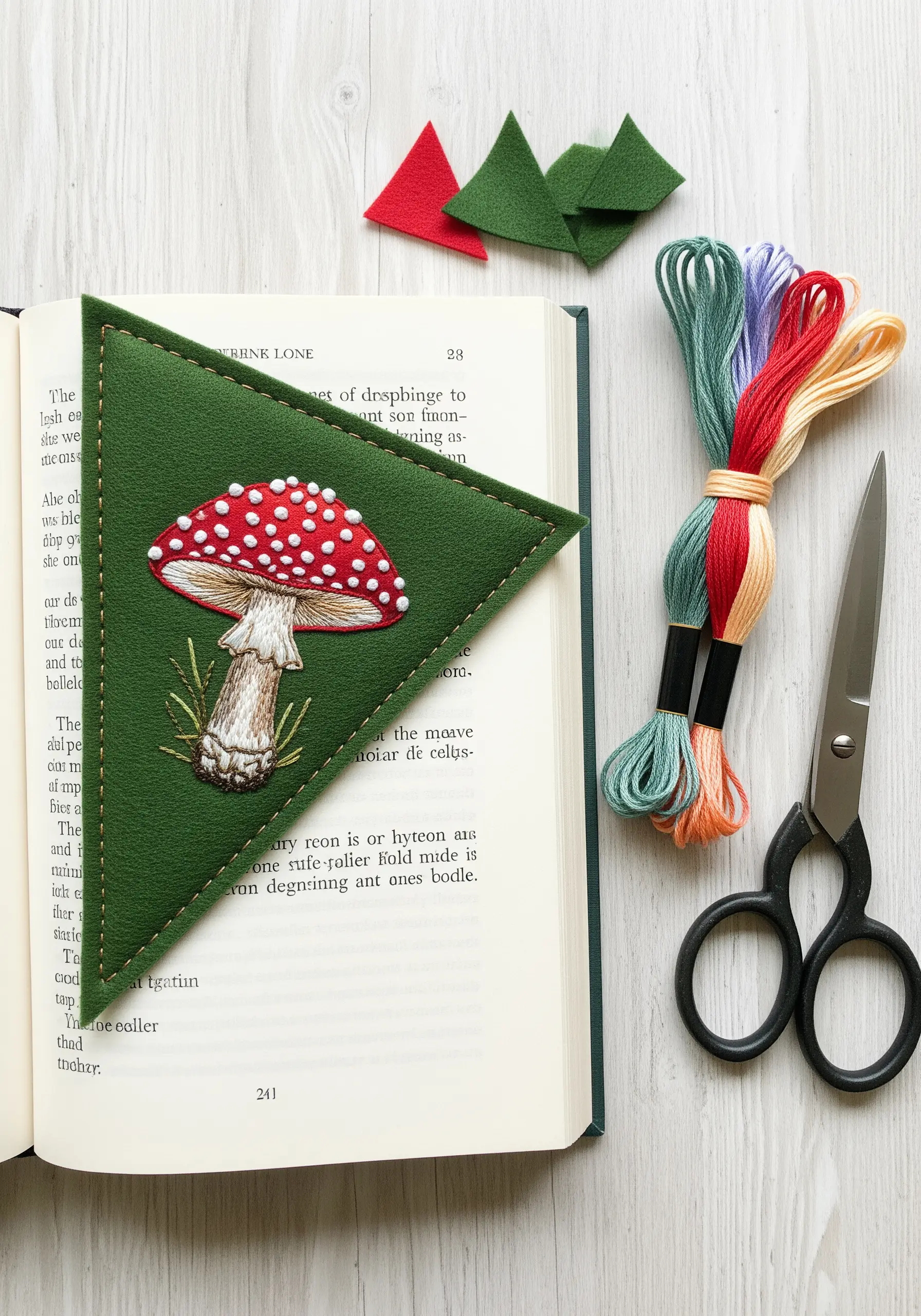 A green felt corner bookmark embroidered with a realistic red-and-white toadstool mushroom.