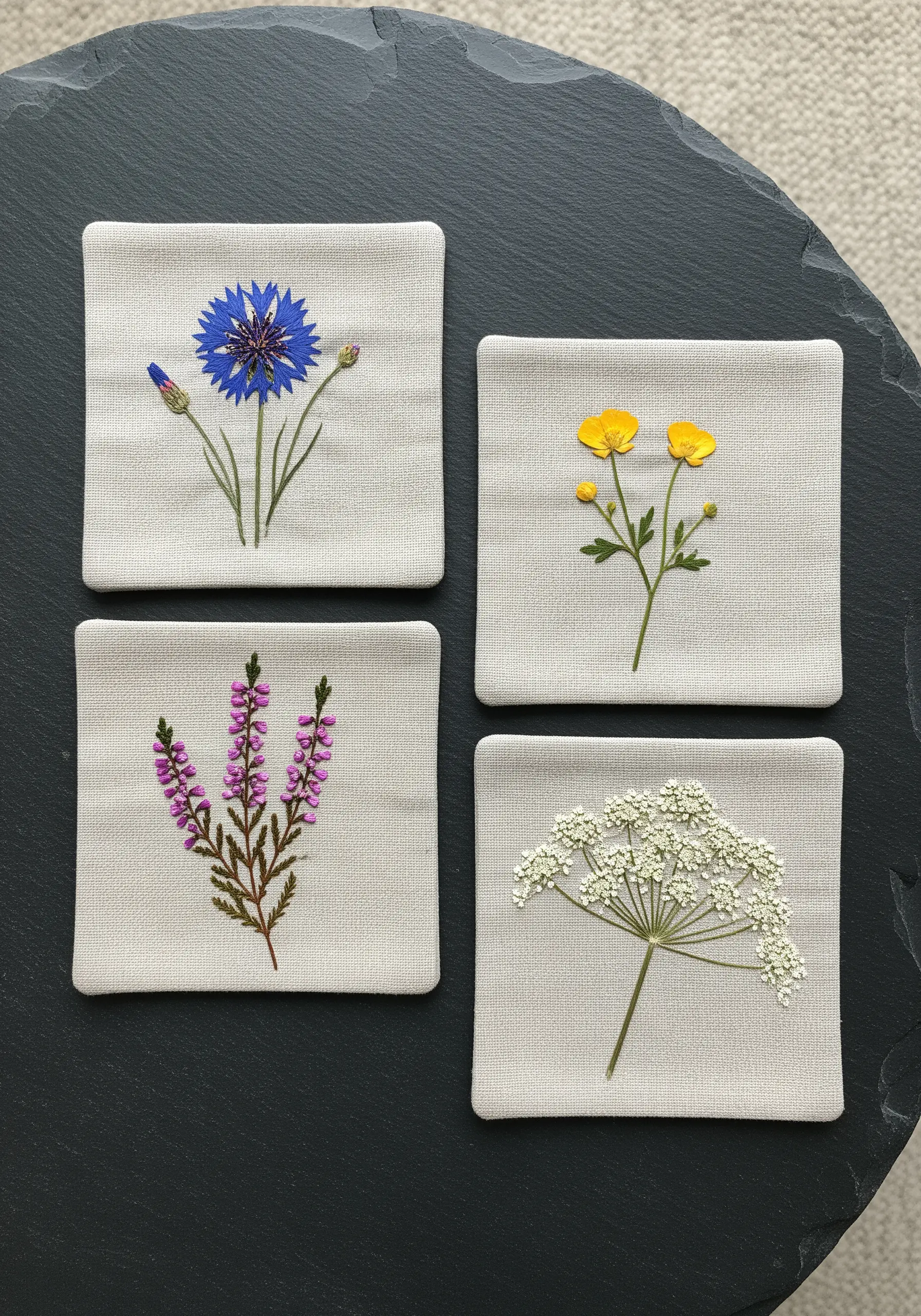 A set of four linen coasters, each embroidered with a different wildflower specimen.