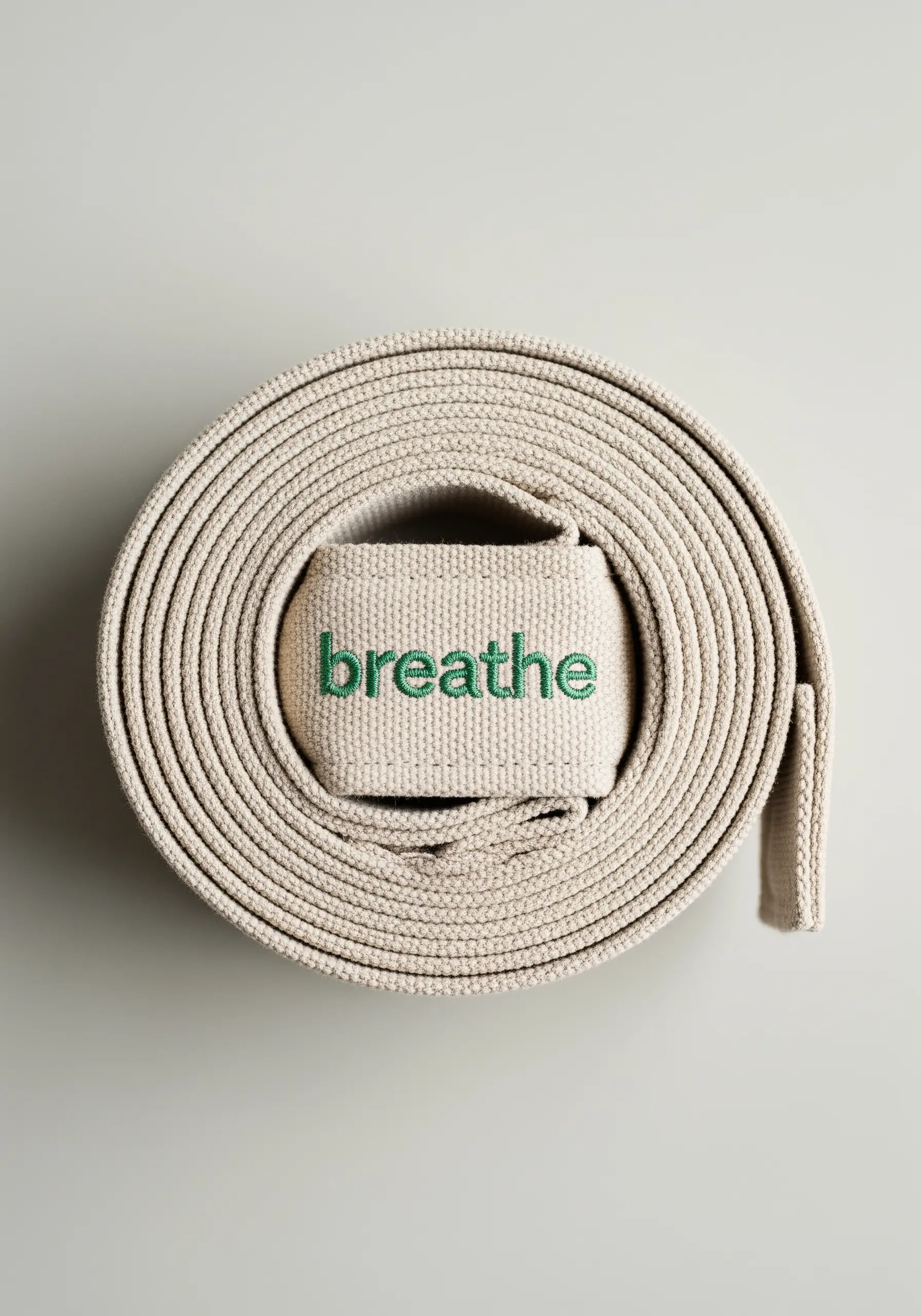The word 'breathe' embroidered in green thread on a coiled canvas yoga strap.