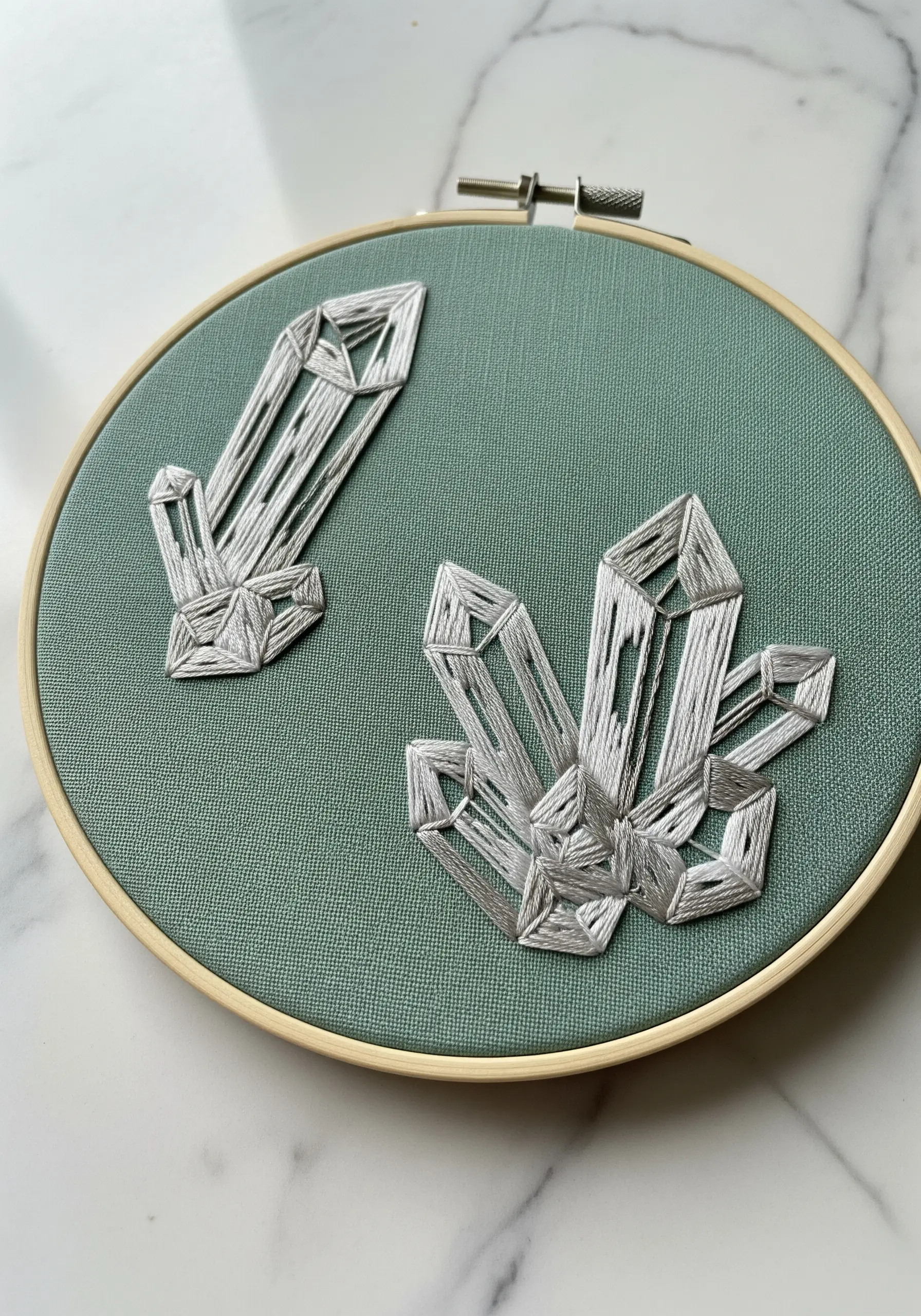 Embroidered crystal formations using directional satin stitch in gray thread on teal fabric.