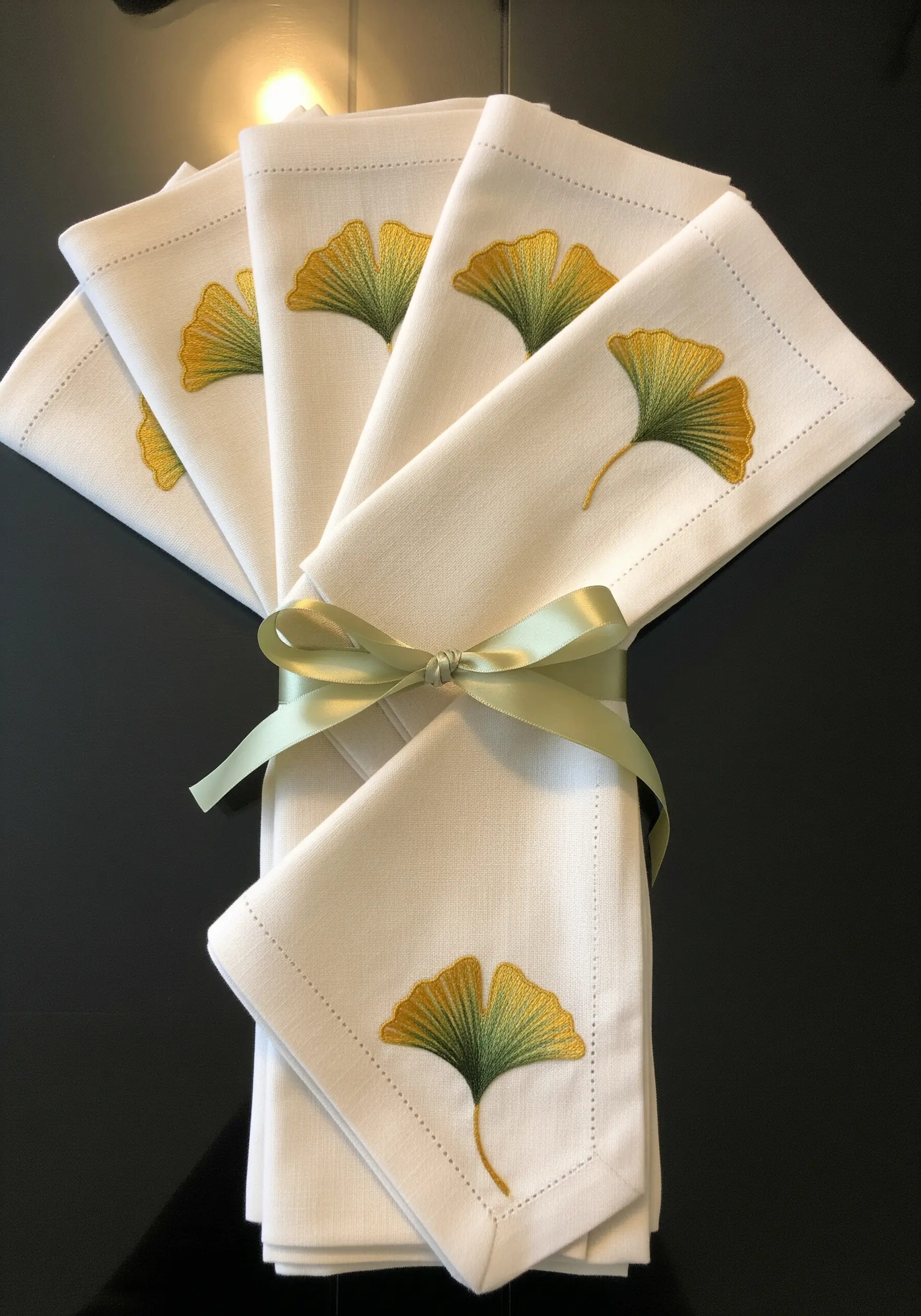 A set of white linen napkins, each embroidered with a delicate, green-and-gold ginkgo leaf.