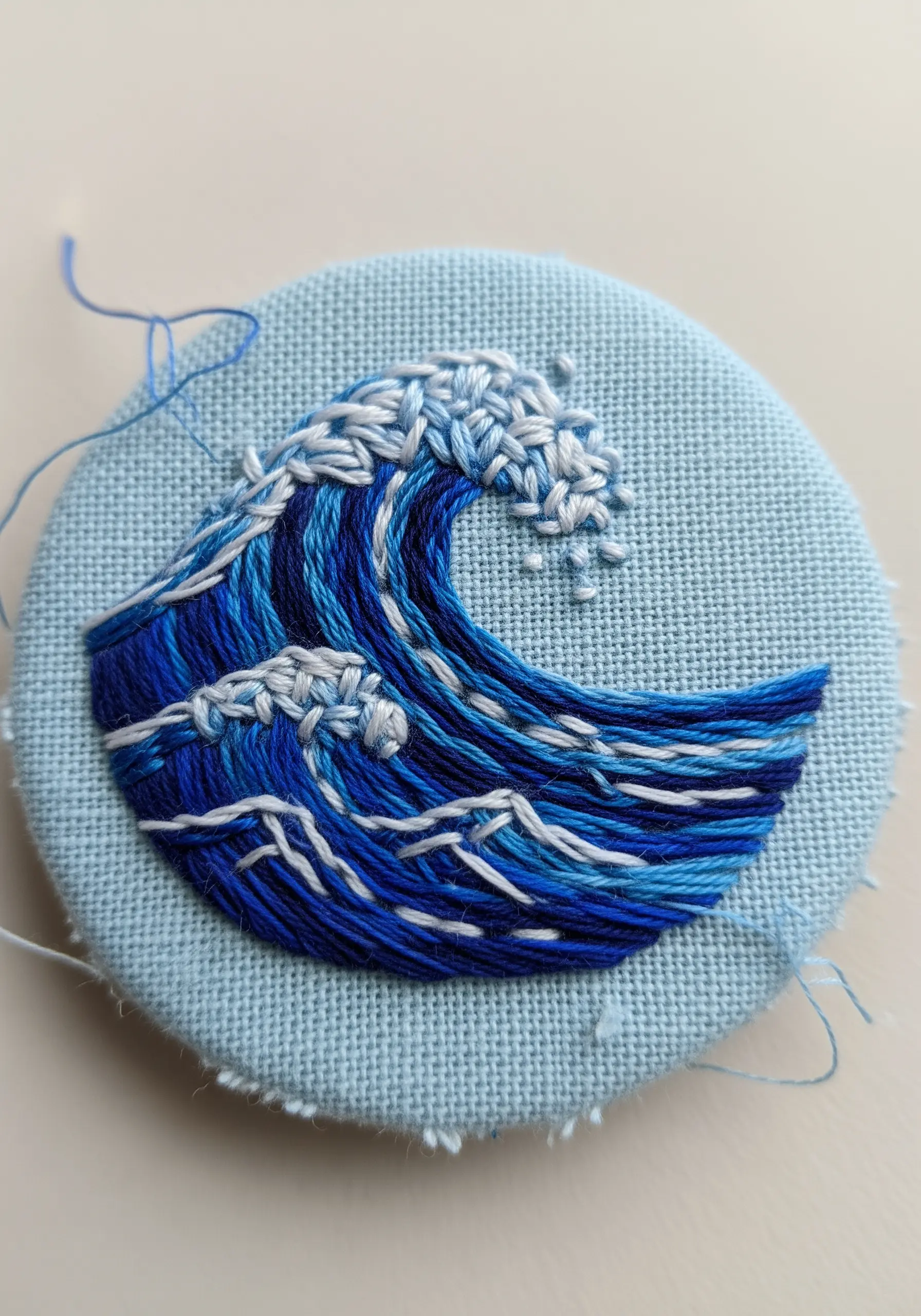 An embroidered wave in various shades of blue, showing movement with different stitches.
